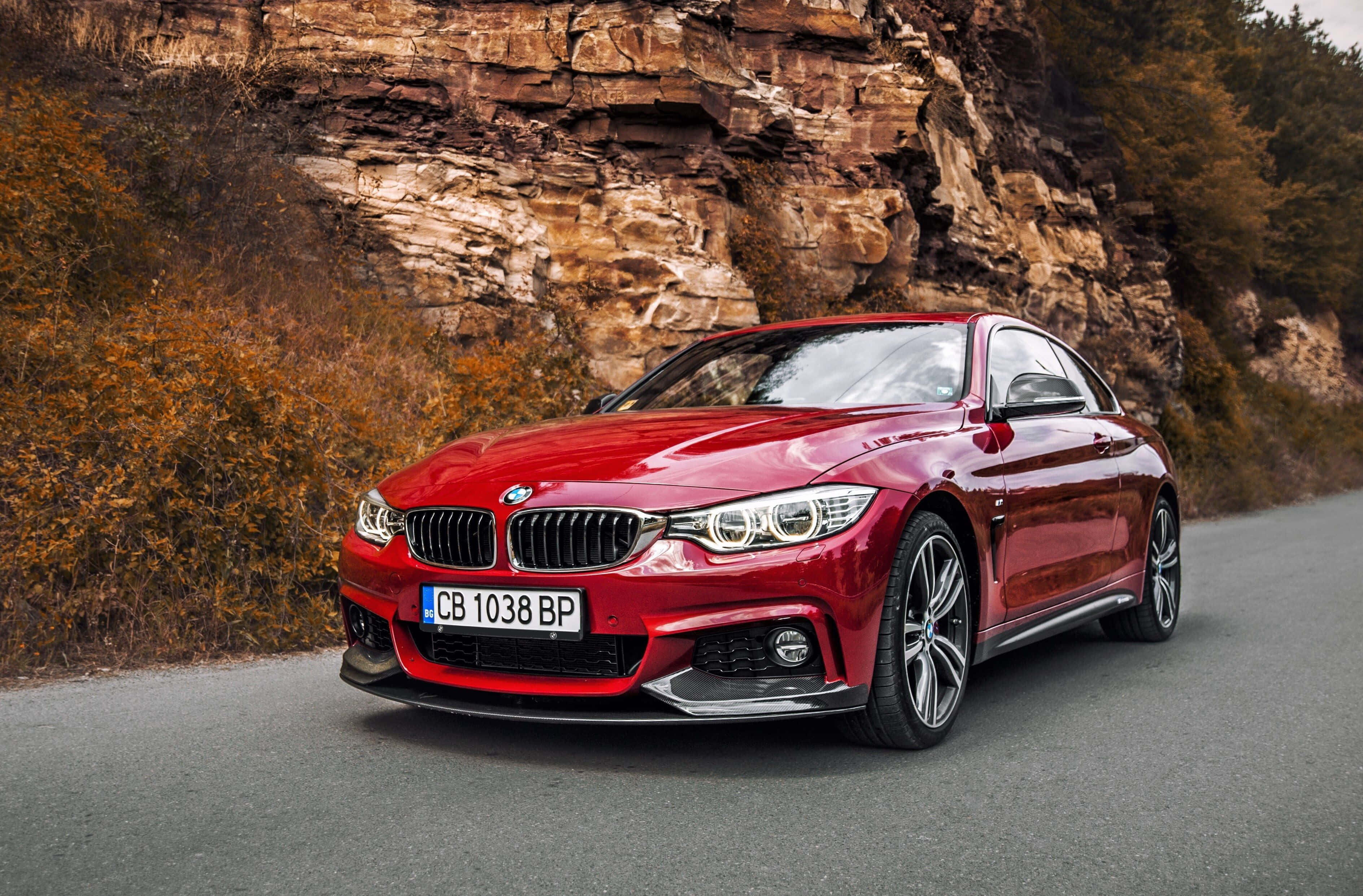 在 BMW 440i 中享受順暢加速體驗 壁紙 — 一輛亮紅色寶馬轎跑車沿著一條蜿蜒的道路行駛，旁邊是佈滿秋葉的崎嶇懸崖。