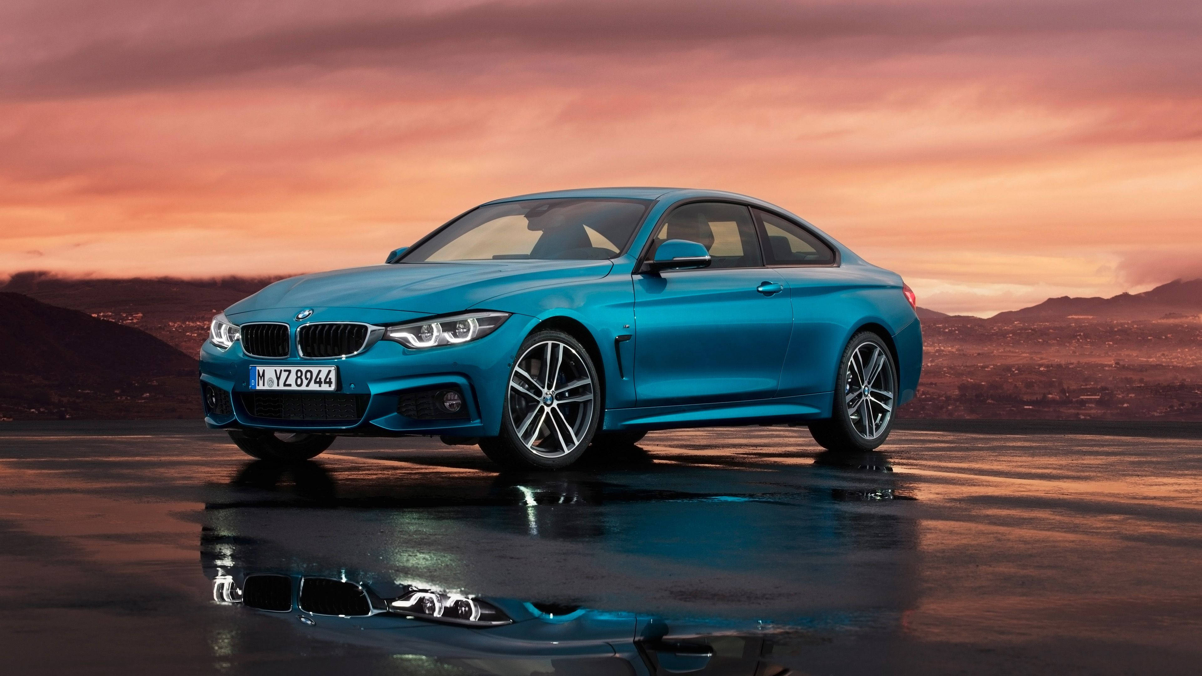 BMW 4系列 Coupe M Sport 壁紙 — 一輛鮮藍色寶馬轎跑車在濕滑的道路上閃閃發光，背景是火燒般的夕陽天空和遠山。