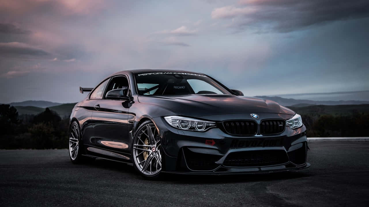BMW 5系列豪華轎車 壁紙 — 一輛時尚的黑色BMW M4雙門轎跑車，配備定制輪轂和空氣動力學車身套件，在黃昏時分停在一條道路上，背景是起伏的丘陵。