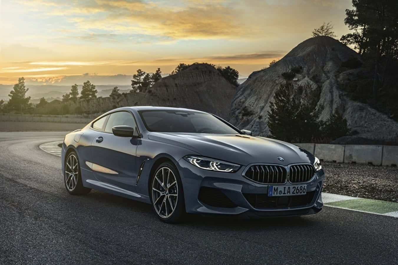灰色BMW 8系列轎跑車在金色日落時分行駛在蜿蜒的山路上。