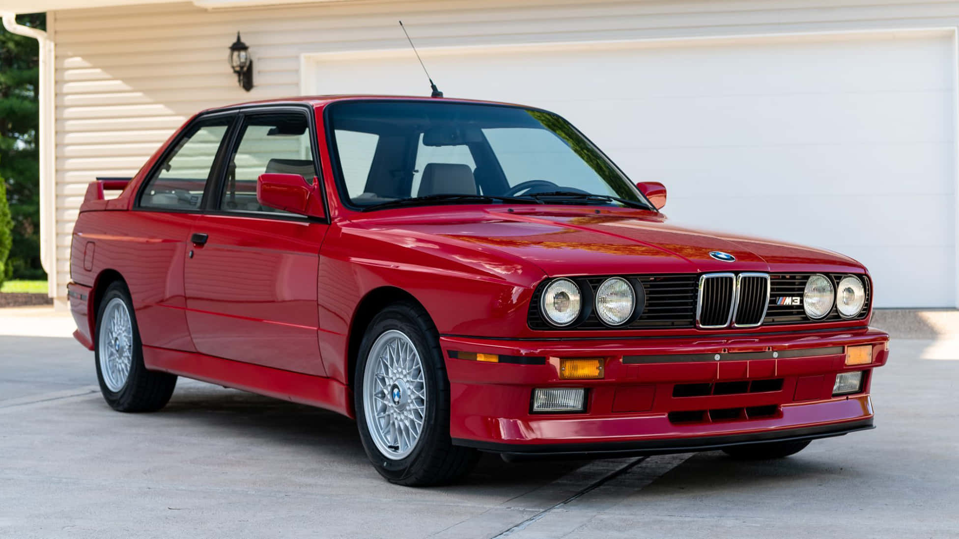 BMW — 奢華、性能與創新 壁紙 — 一輛光亮的紅色BMW M3跑車停泊在白色車庫前的混凝土車道上。