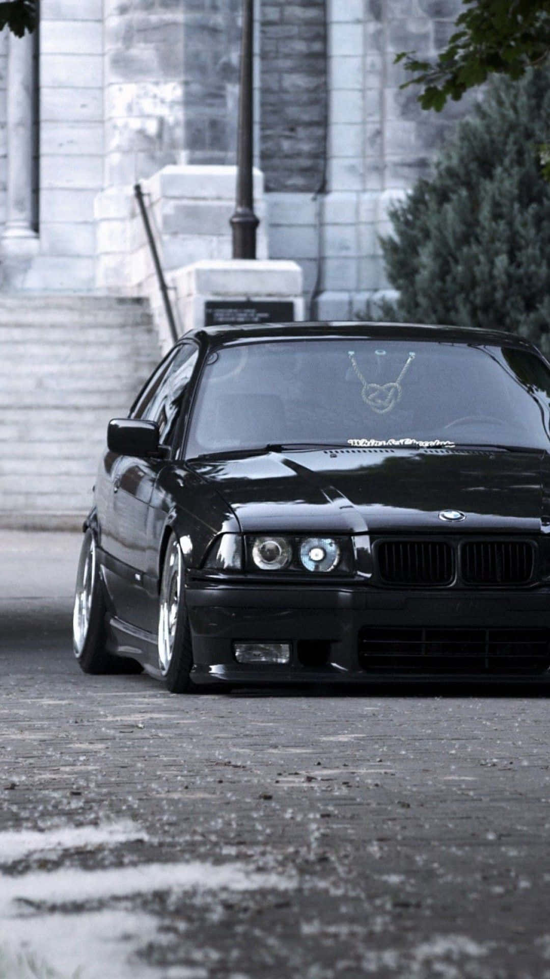 黑色BMW E36停泊在石建築附近濕漉漉的鵝卵石街道上。
