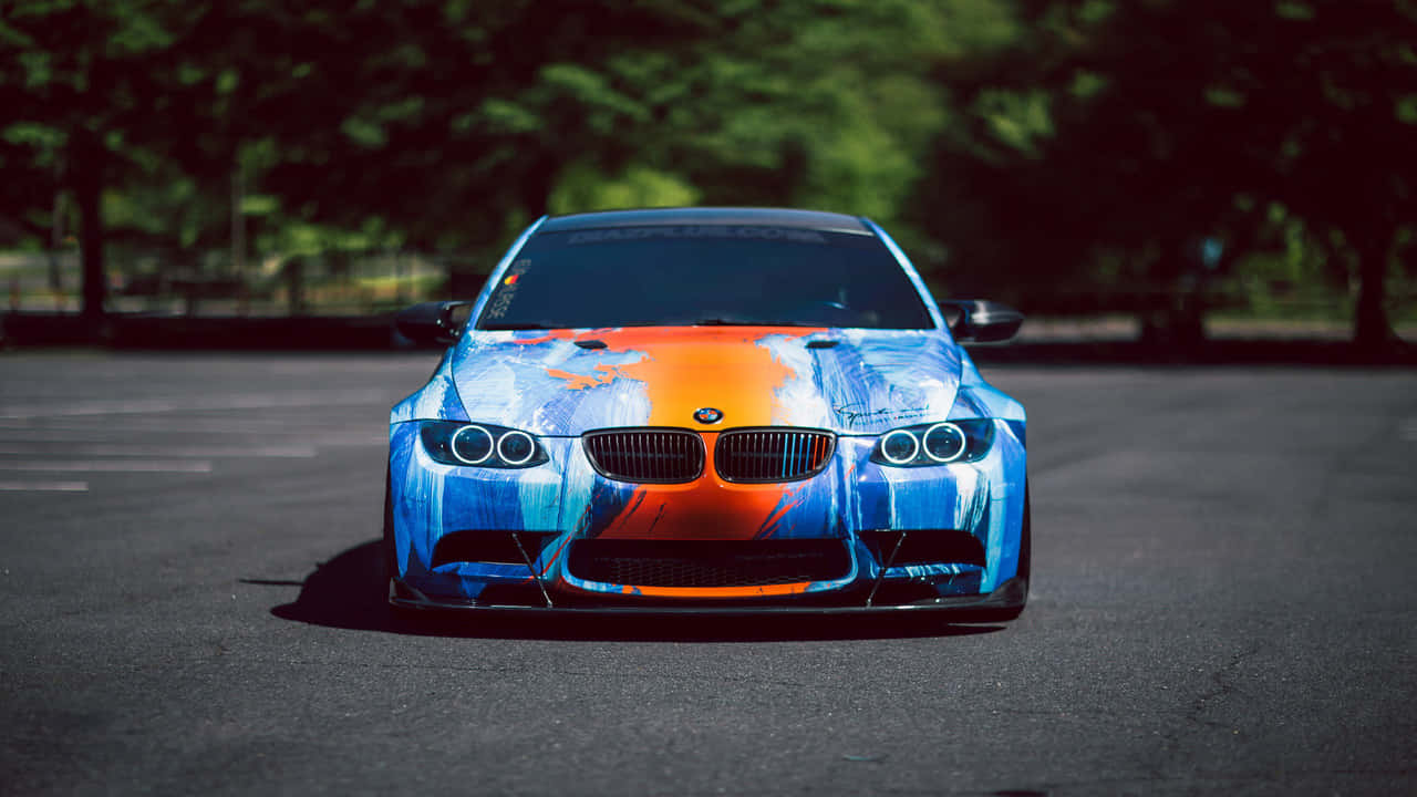奢華之巔：BMW 壁紙 — 一輛BMW跑車帶有鮮明的藍色和橙色塗鴉風格塗裝，停在樹下的瀝青路面上。
