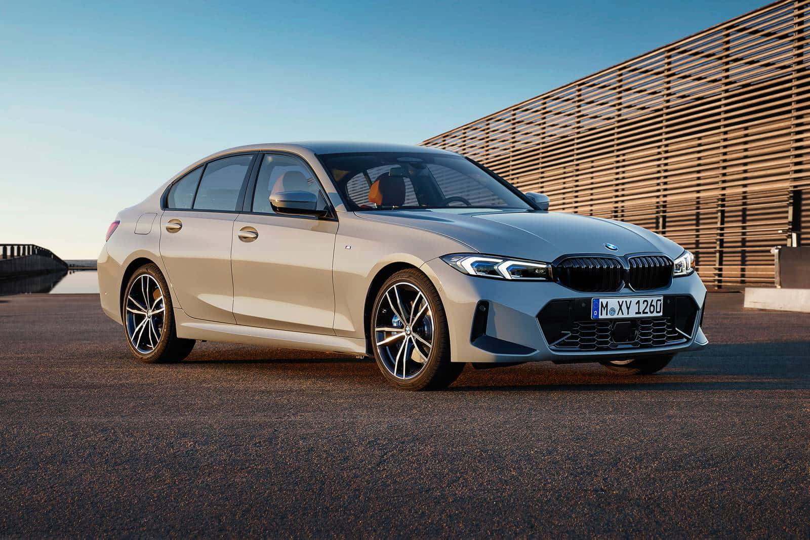體驗BMW的力量 壁紙 — 一架時尚的銀色寶馬3系房車停泊在瀝青路上，旁邊是木條牆，上方是清澈的藍天。