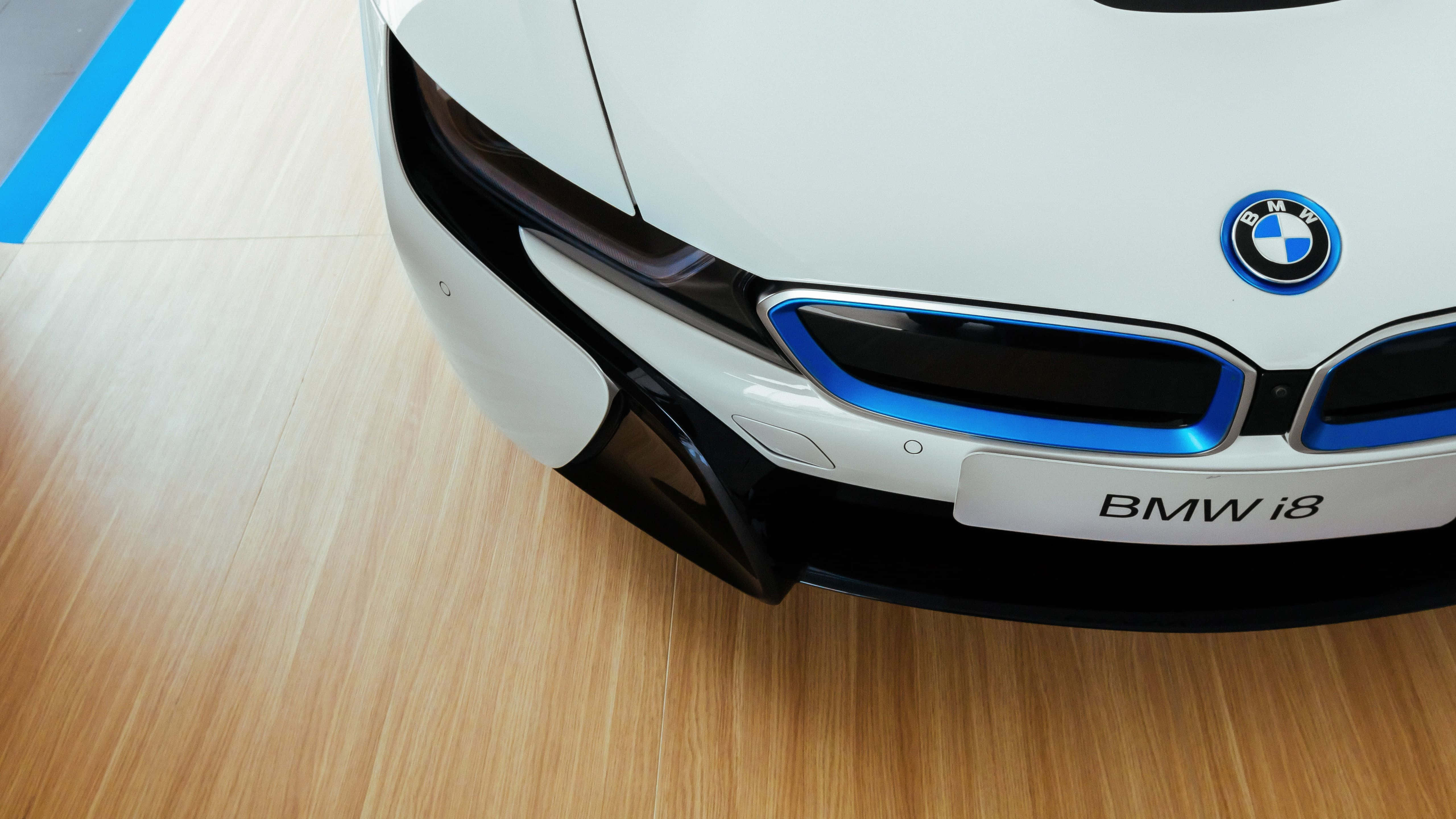 BMW i8混合動力車型平板壁紙 壁紙 — 白色BMW i8未來感前格柵特寫，在淺色木地板上帶有發光藍色飾邊。