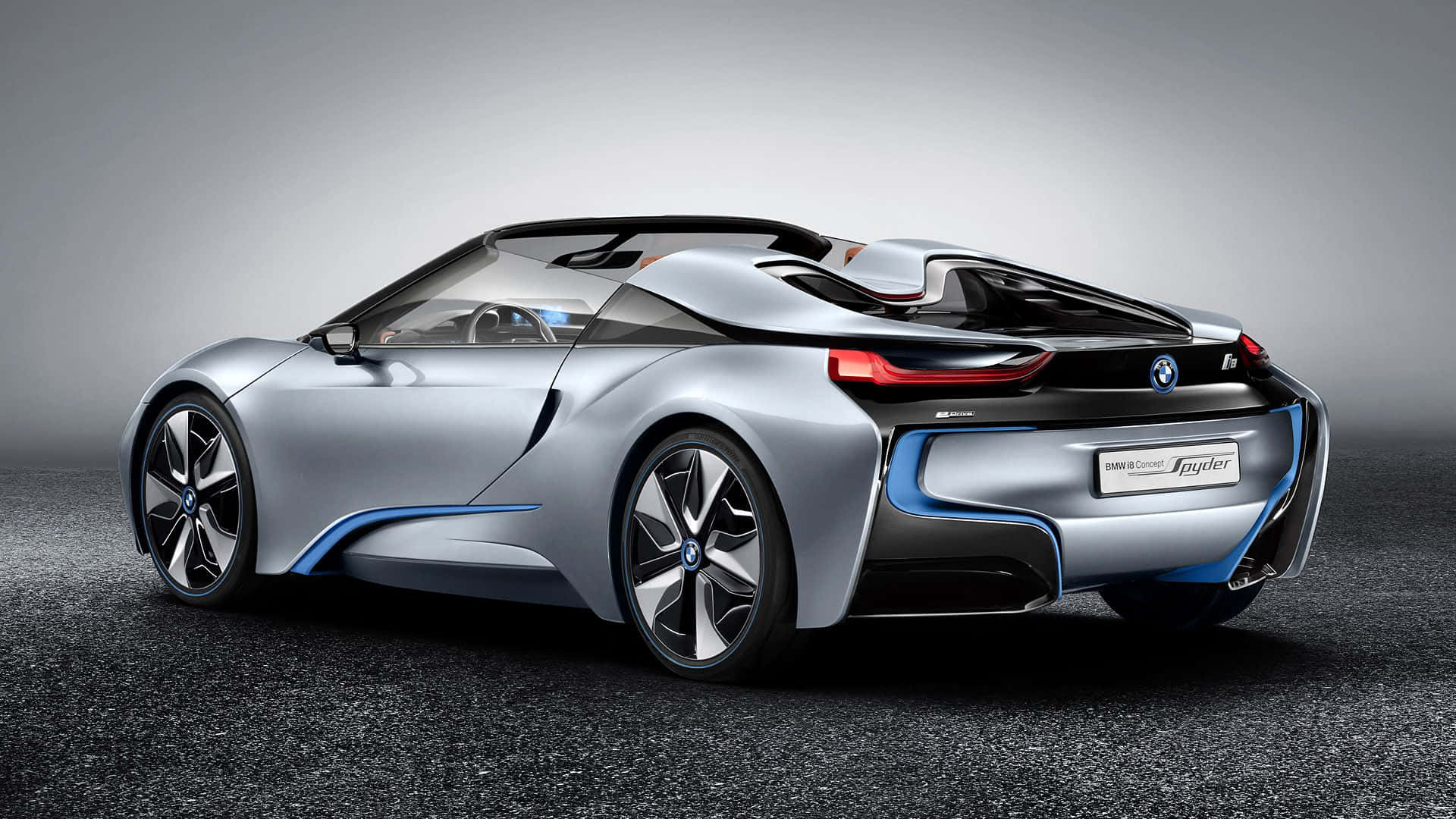 BMW 桌面 i8 運動跑車 壁紙 — 一輛時尚的銀色BMW i8 Spyder概念車，帶有藍色飾條和紅色尾燈，從後方四分之三視角展示在深色紋理表面上，背景為漸變灰色。
