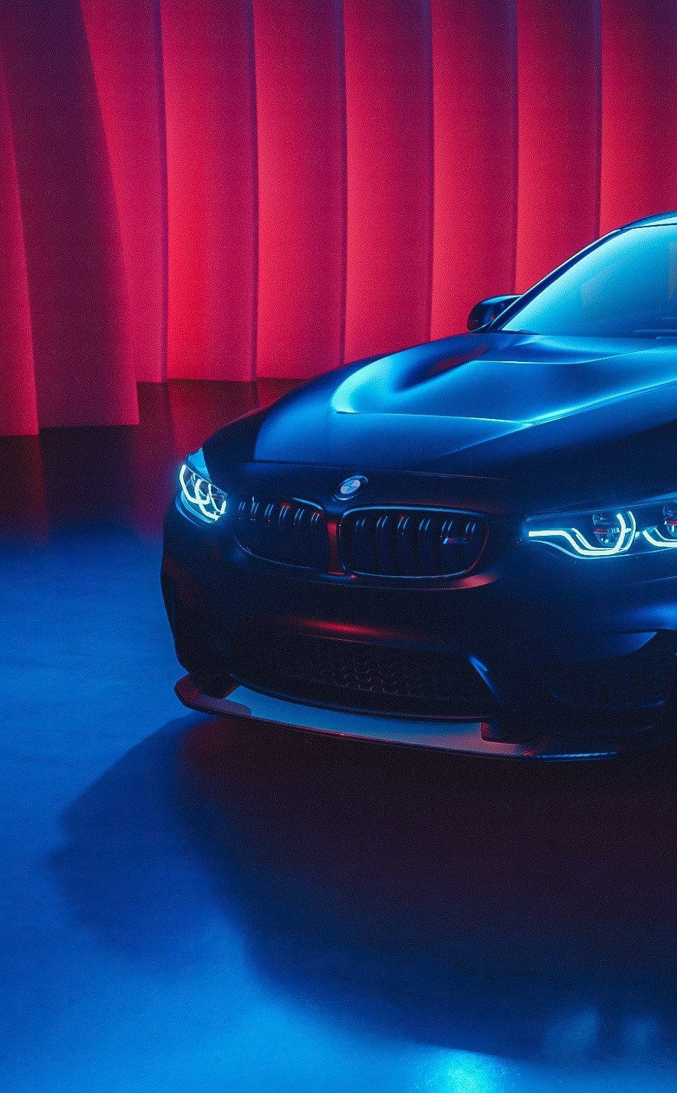 BMW iPhone X M4車型 壁紙 — 一輛時尚的黑色BMW跑車在戲劇性的紅藍色工作室燈光下，以窗簾為背景閃耀著光芒。