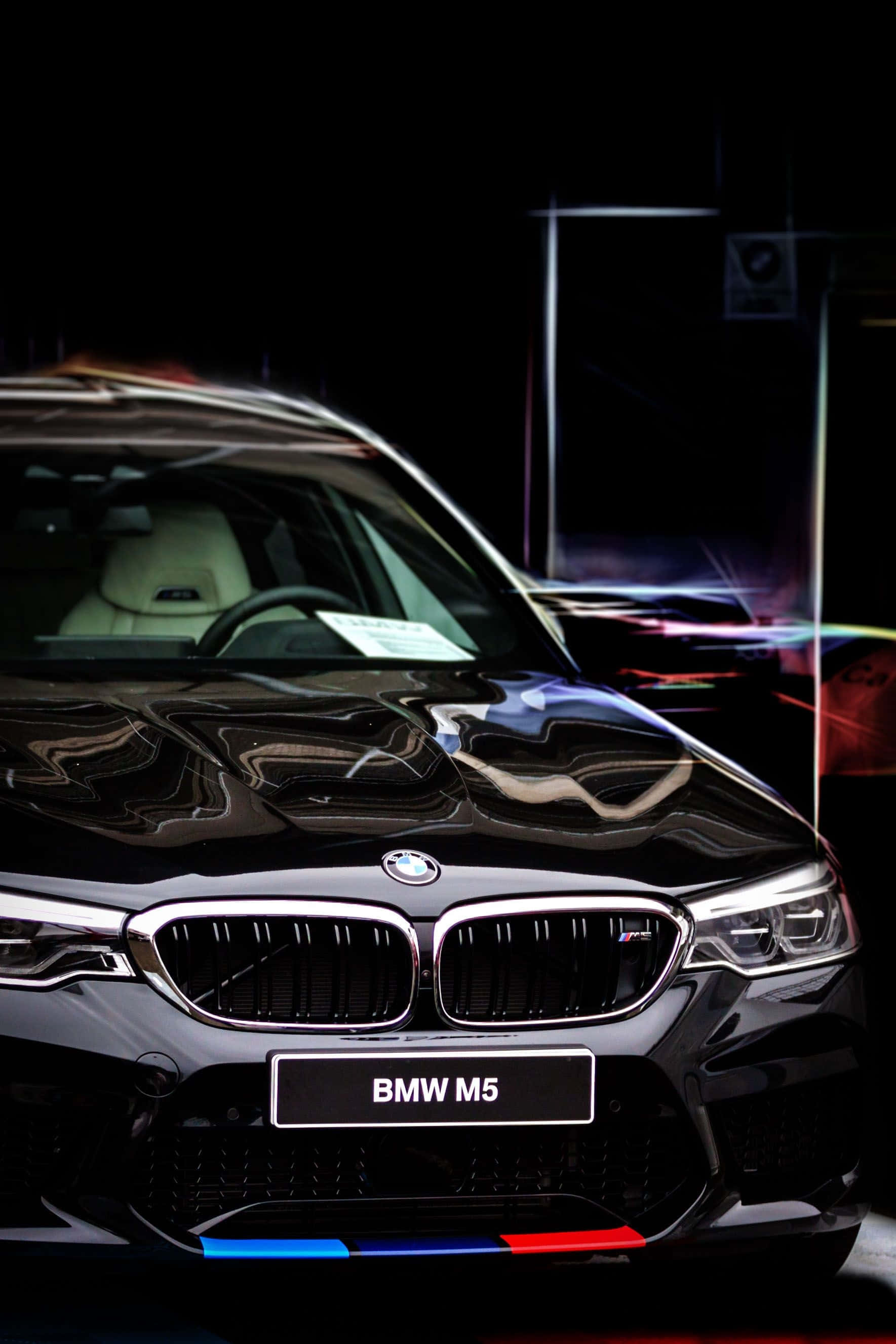 駕馭BMW，體驗時尚現代的駕駛樂趣 壁紙 — 一架時尚的黑色BMW M5跑車在戲劇性的攝影棚燈光下閃耀，背景中充滿活力的霓虹反射。