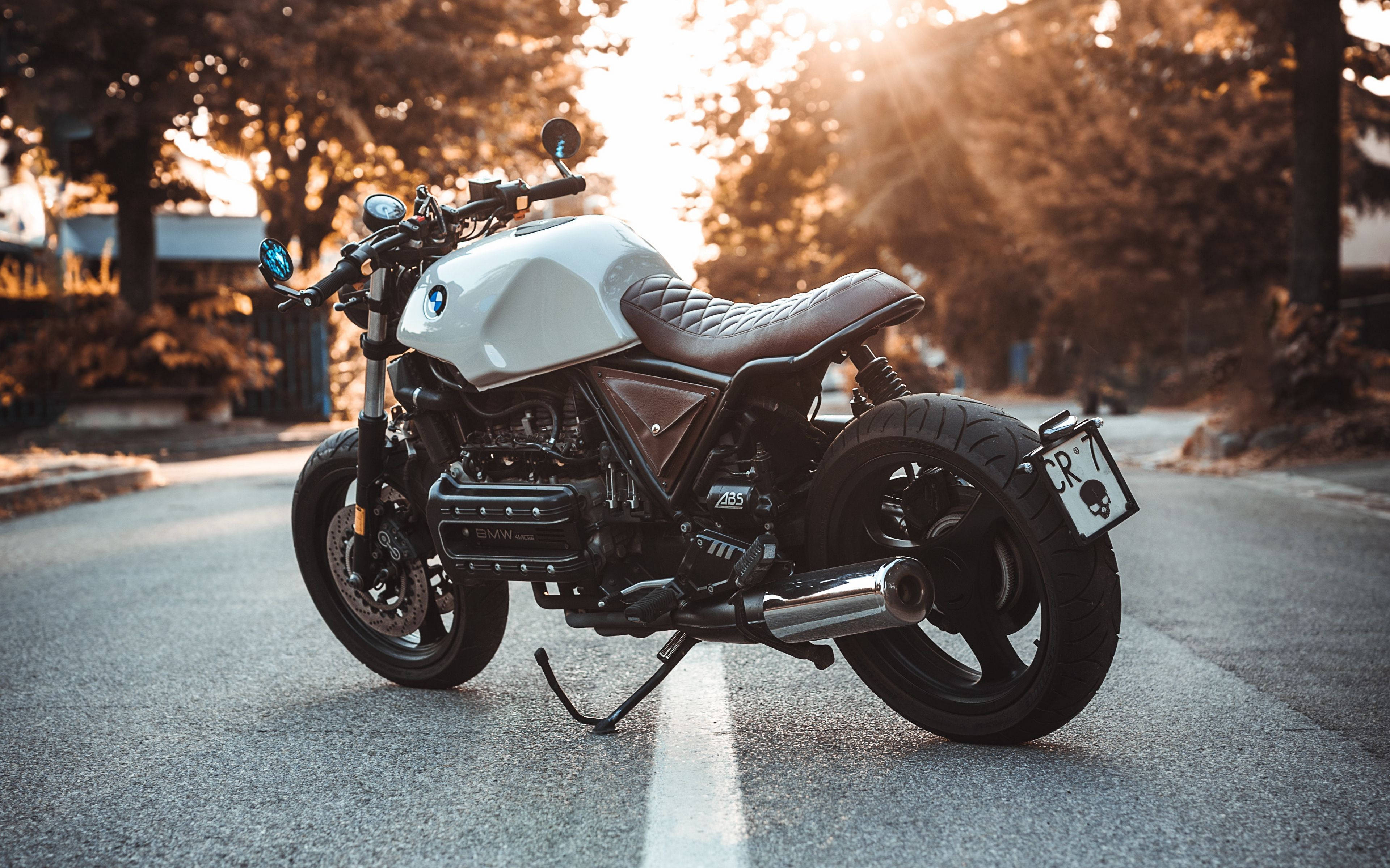 BMW K100 4K機車 壁紙 — 一架白色定制電單車停泊在陽光普照的道路上，樹木和溫暖的金色光線穿過。