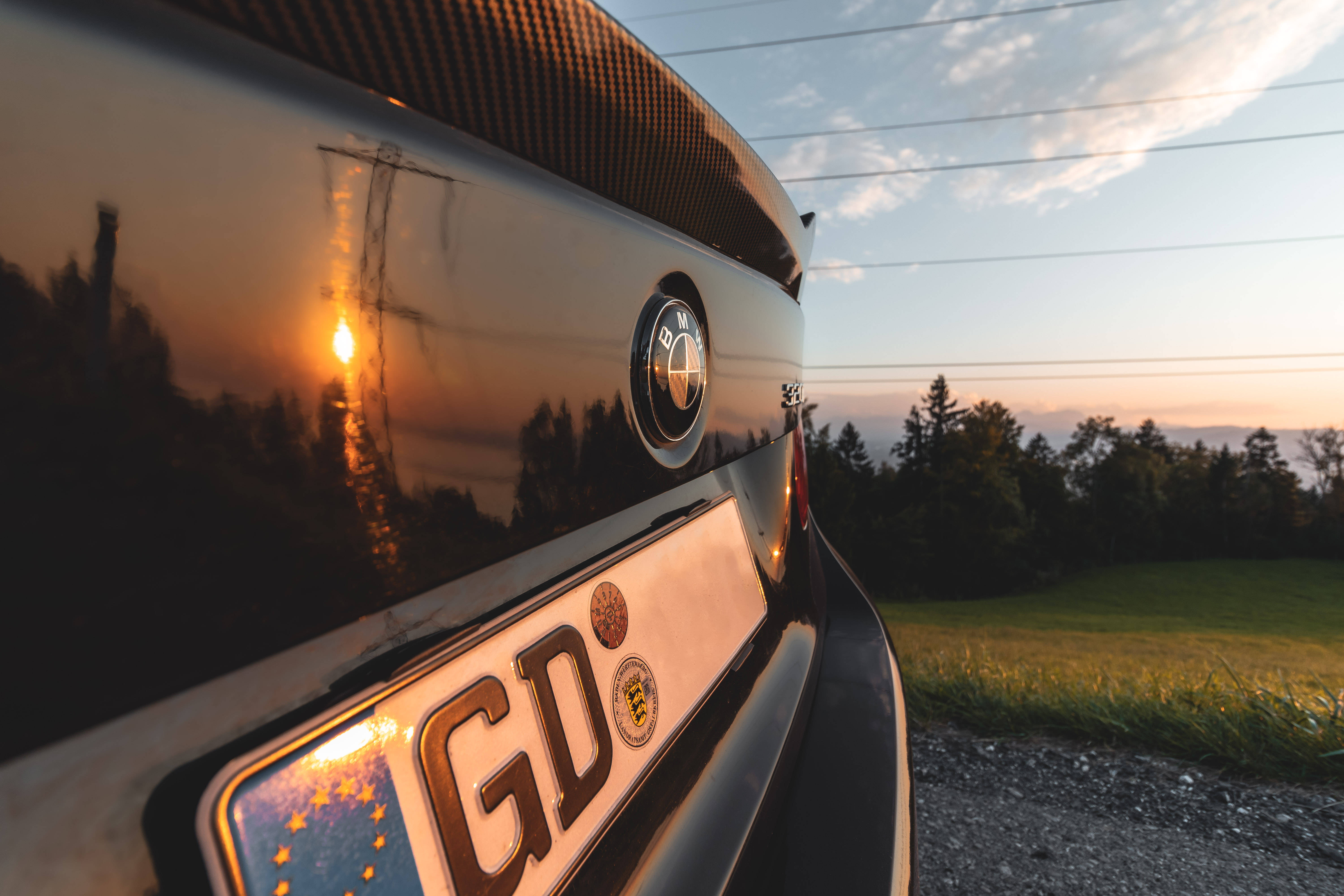 BMW M系列車尾 壁紙 — 日落時黑色寶馬汽車尾部的特寫，在光滑表面上反射出金色天空和樹木。