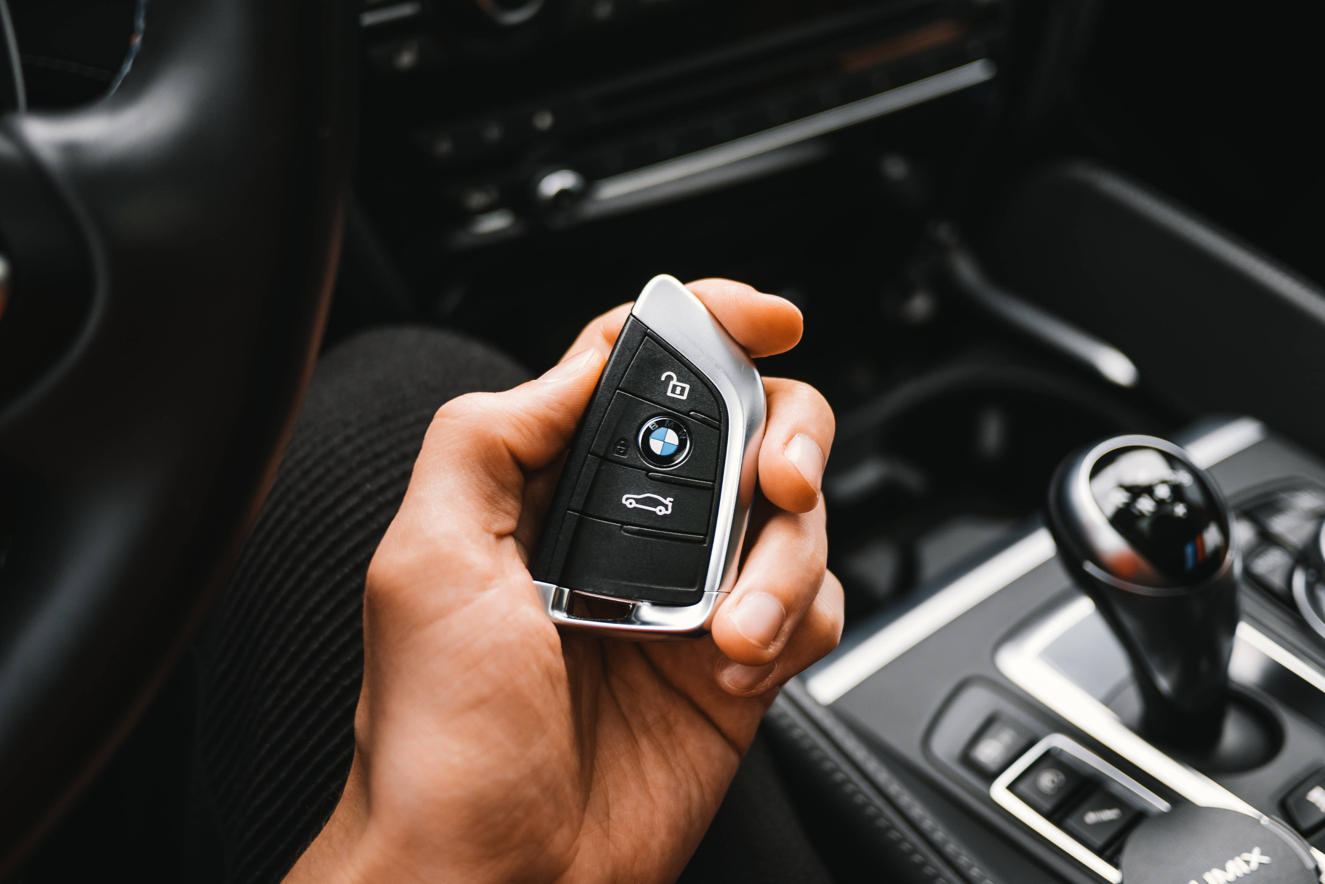 無鑰匙黑白色BMW M遙控器 壁紙 — 一隻手握住寶馬車匙遙控器，在時尚的黑色車廂內，可見波棍。
