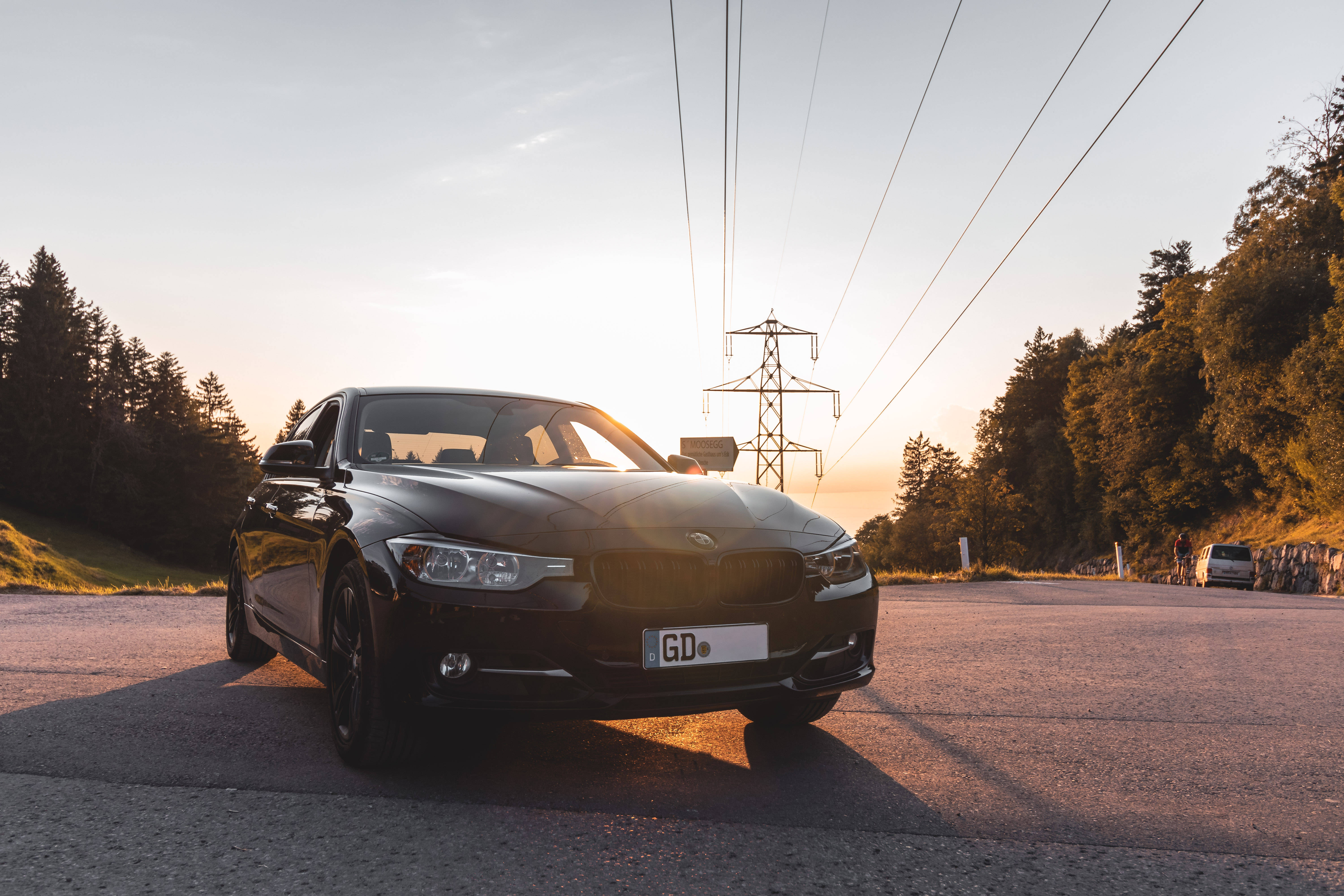 黑色BMW M系列 壁紙 — 一架時尚的黑色寶馬房車停泊在日落時分蜿蜒的山路上，背景有電線和樹木。
