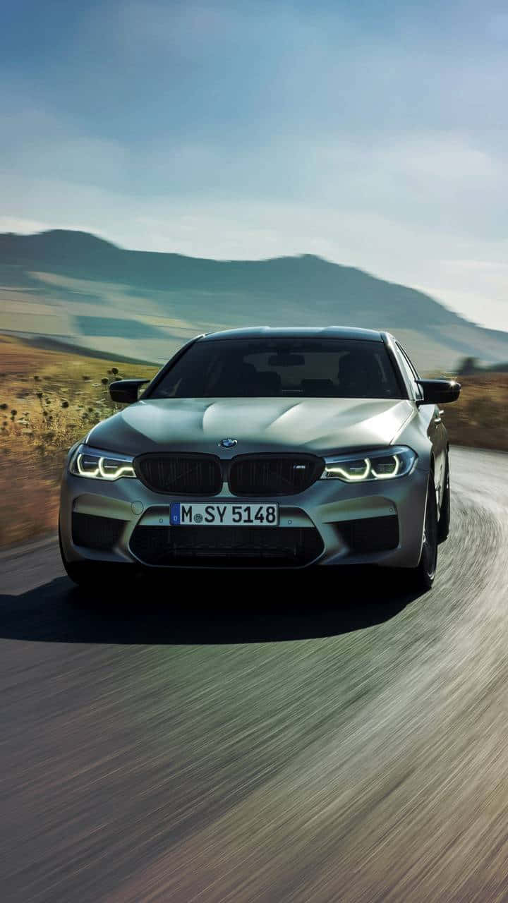 銀色BMW M5在日落時分沿著蜿蜒道路穿過丘陵地帶疾馳。