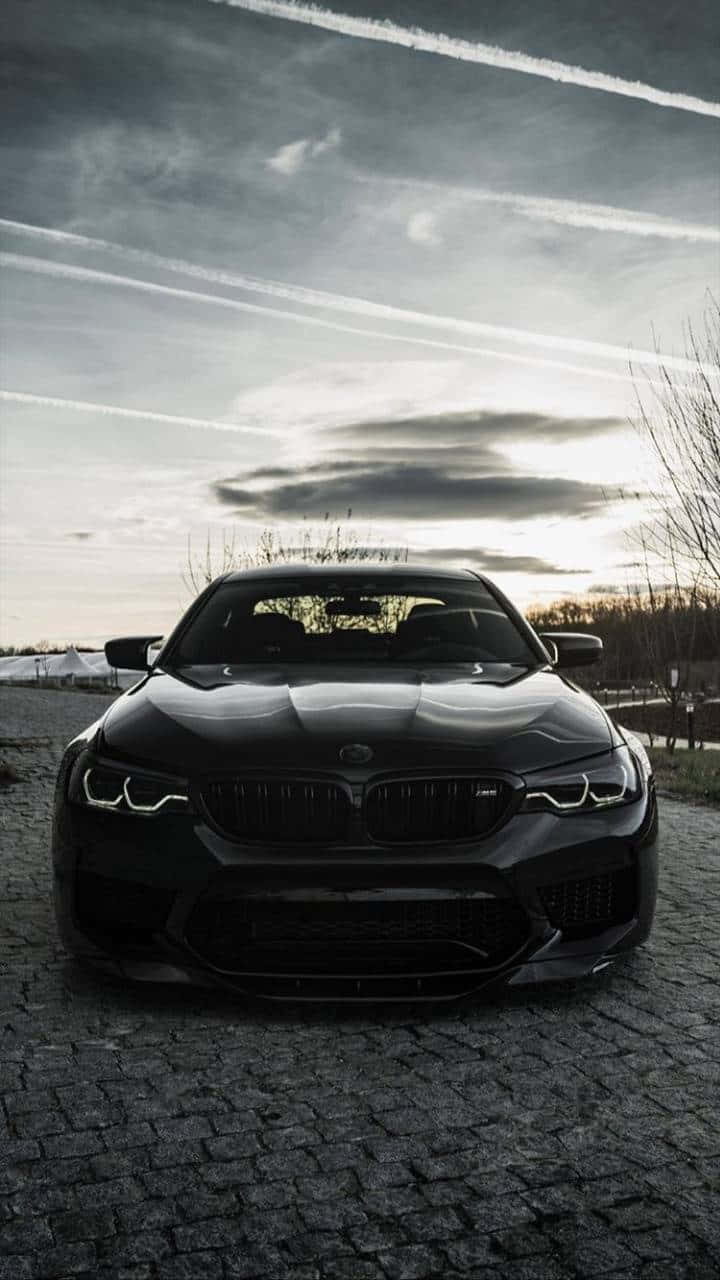 夕陽下鵝卵石路上的黑色BMW M5，天空戲劇性。