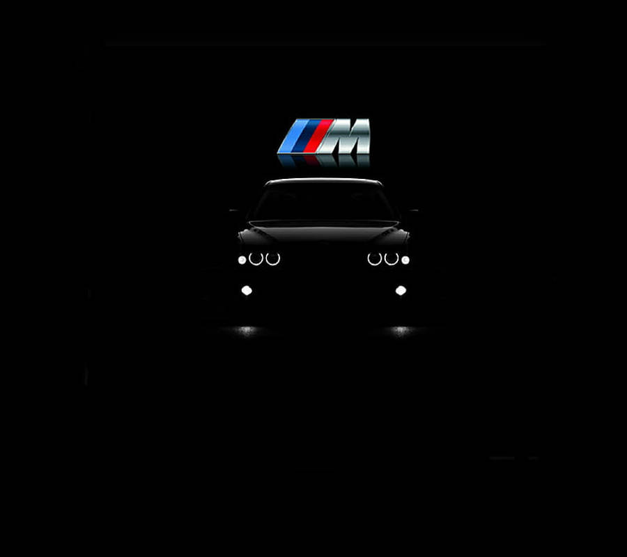 BMW M系列細節 - 精準工程的體現 壁紙 — 一架時尚的BMW M車剪影在漆黑背景中閃爍著車頭燈，頂部有一個發光的M標誌。