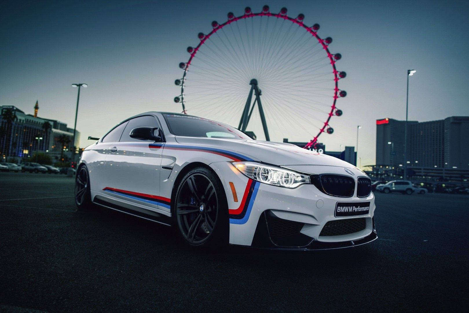 BMW M 系列性能車 壁紙 — 一輛帶有紅色、藍色和橙色賽車條紋的白色BMW M4雙門跑車，在黃昏時停放在倫敦眼前面。