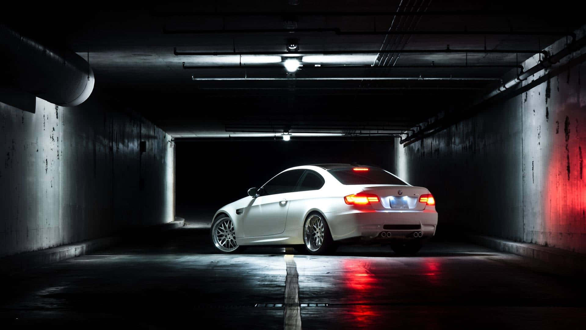 BMW M3 GT2 穿過隧道 1920x1080 M系列背景 壁紙 — 一架時尚白色跑車，紅色尾燈發光，停泊在燈光昏暗、混凝土地面潮濕、帶工業照明的地下停車場。