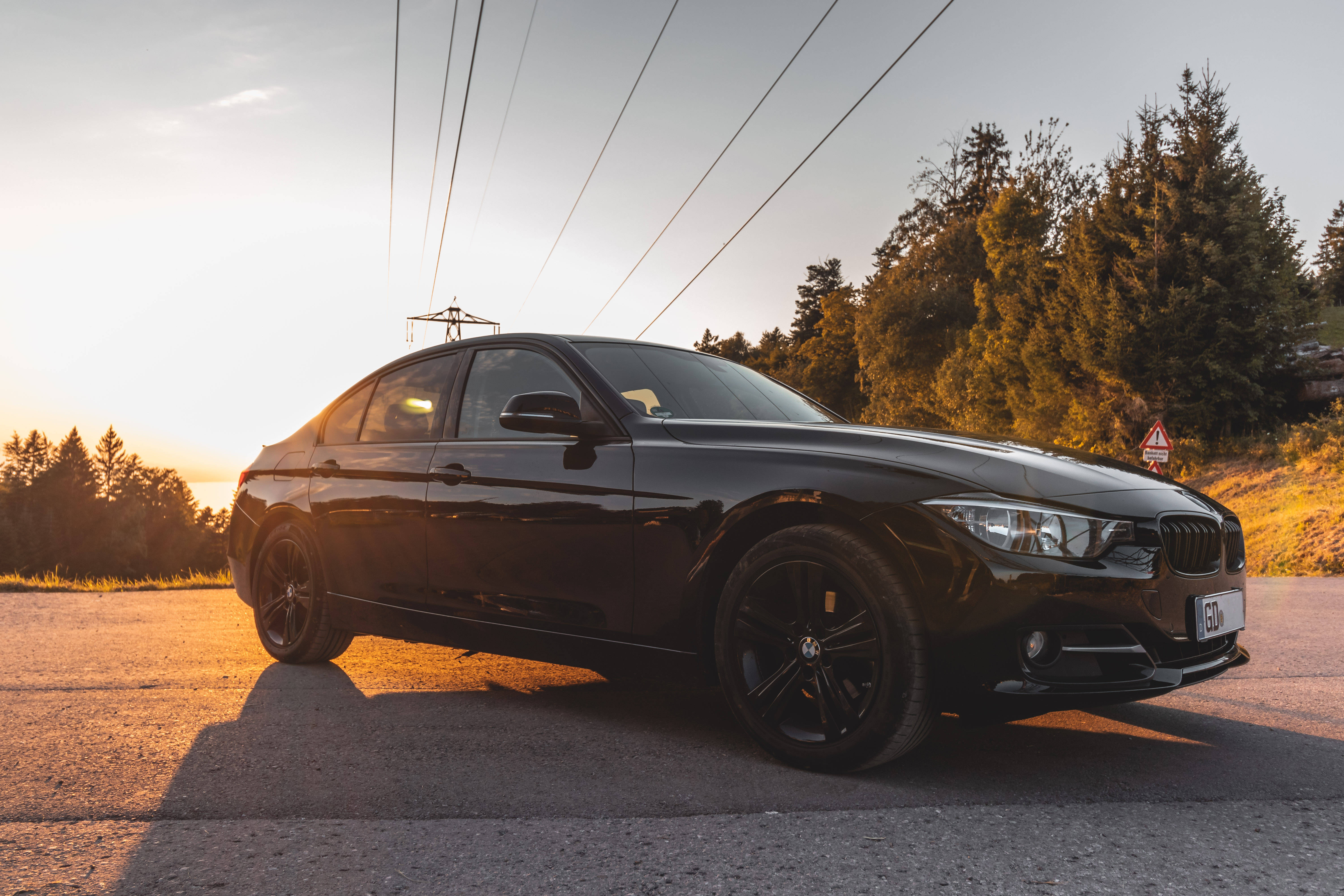 BMW M3系列跑車 壁紙 — 一架時尚的黑色寶馬房車停泊在日落時分的陽光路上，背景有樹木和電線。
