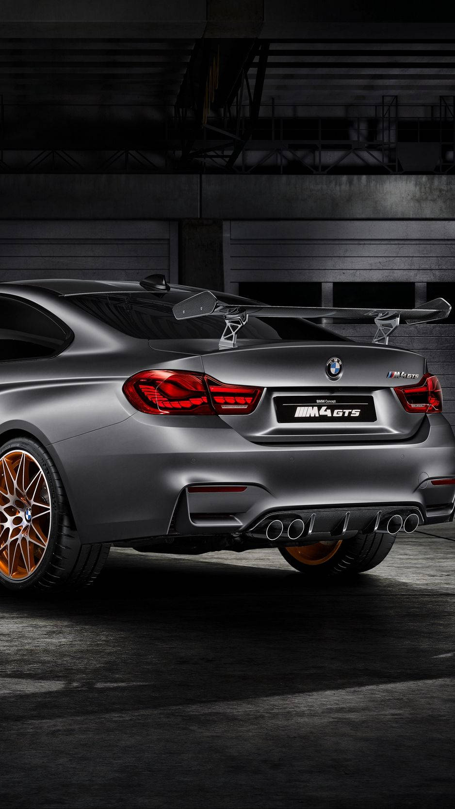 昏暗工業車庫中的啞光灰色BMW M4 GTS，配備銅色輪圈。