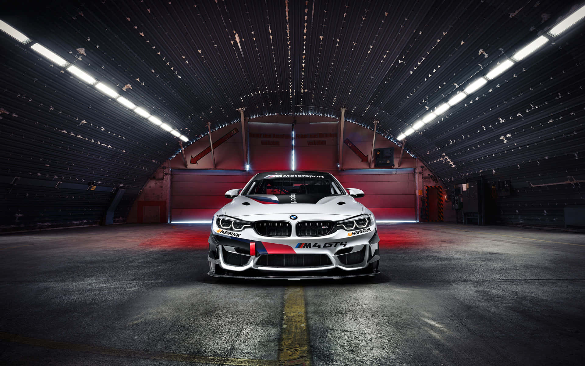 白色BMW M4 GT4賽車在黑暗的工業車庫中，帶有紅色燈光點綴。