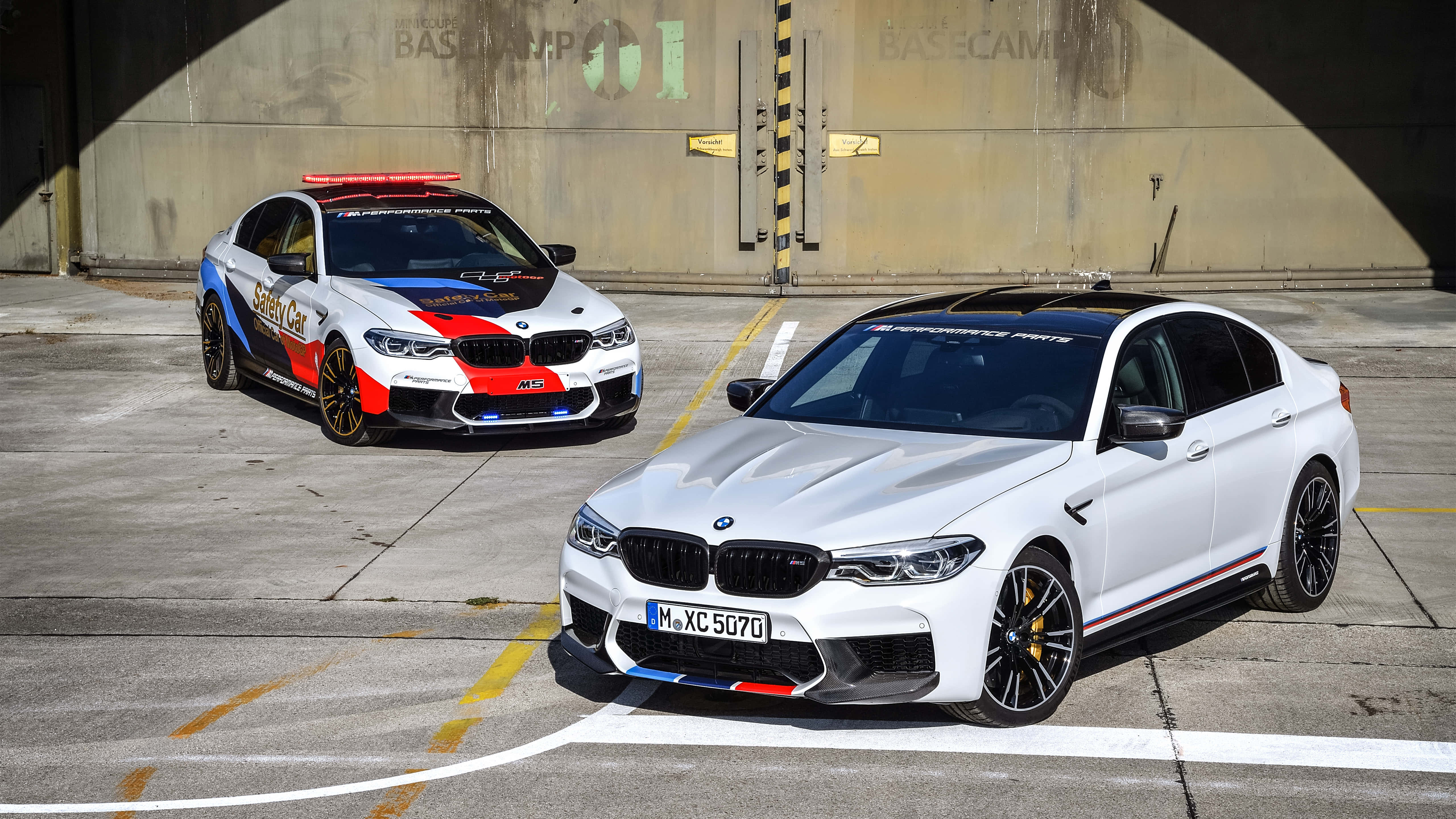 體驗駕駛 BMW M5 的刺激快感 壁紙 — 兩輛高性能BMW M5停放在混凝土車庫中，一輛白色，一輛紅藍安全車。