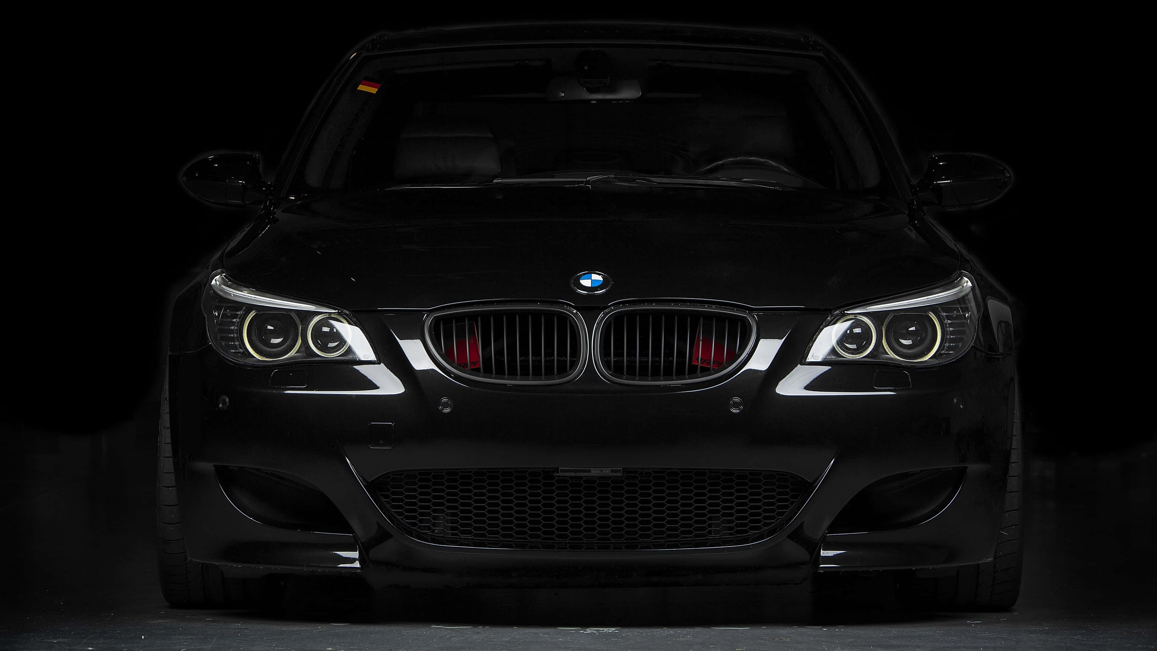 BMW M5黑色車型平板壁紙 壁紙 — 一架流線型黑色BMW跑車在漆黑的工作室背景中亮起車頭燈。
