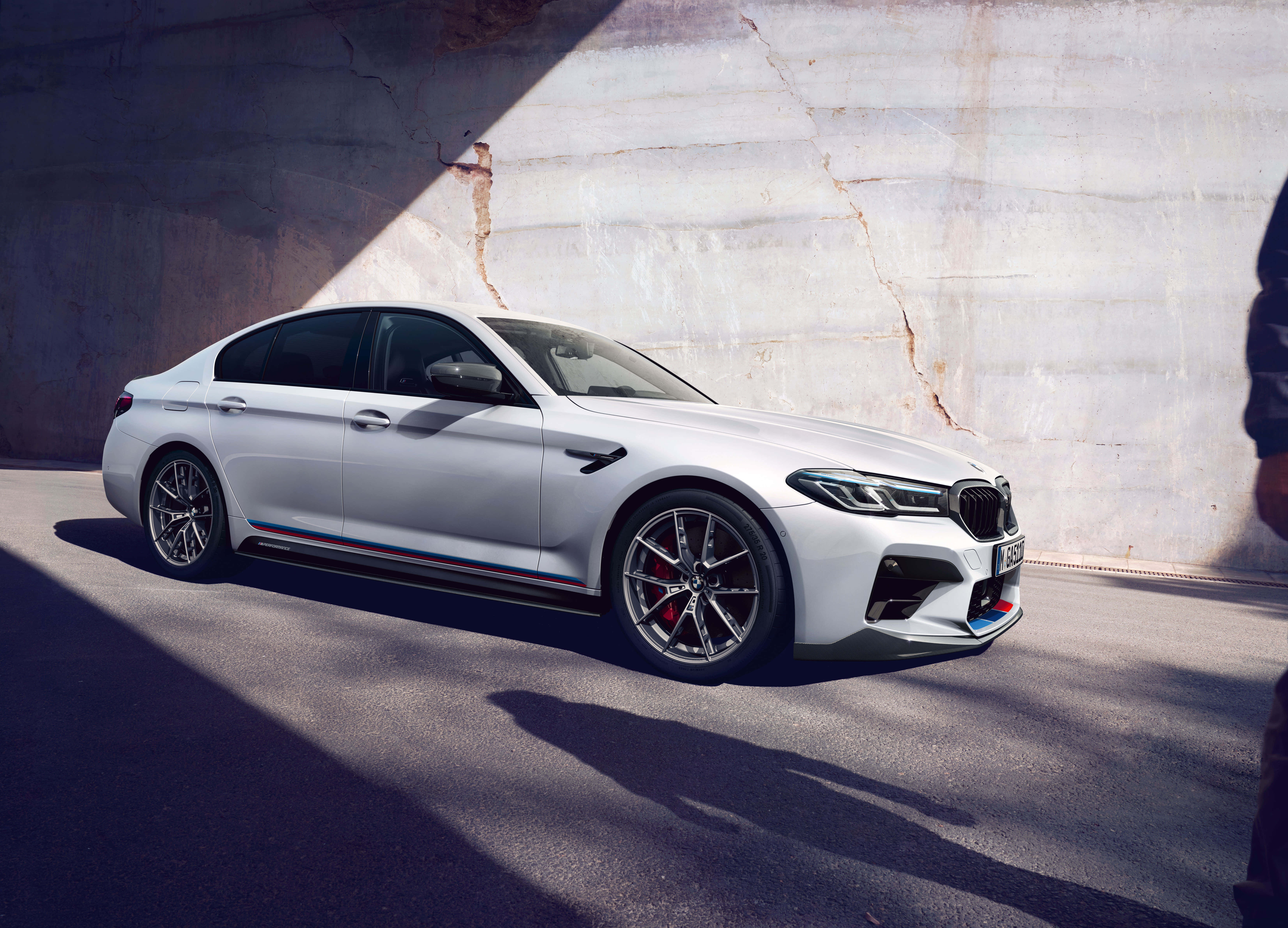 豪華與力量在 BMW M5 中完美結合 壁紙 — 一架時尚的白色BMW M5跑車停泊在混凝土天橋下，戲劇性的陽光投射出銳利的陰影。