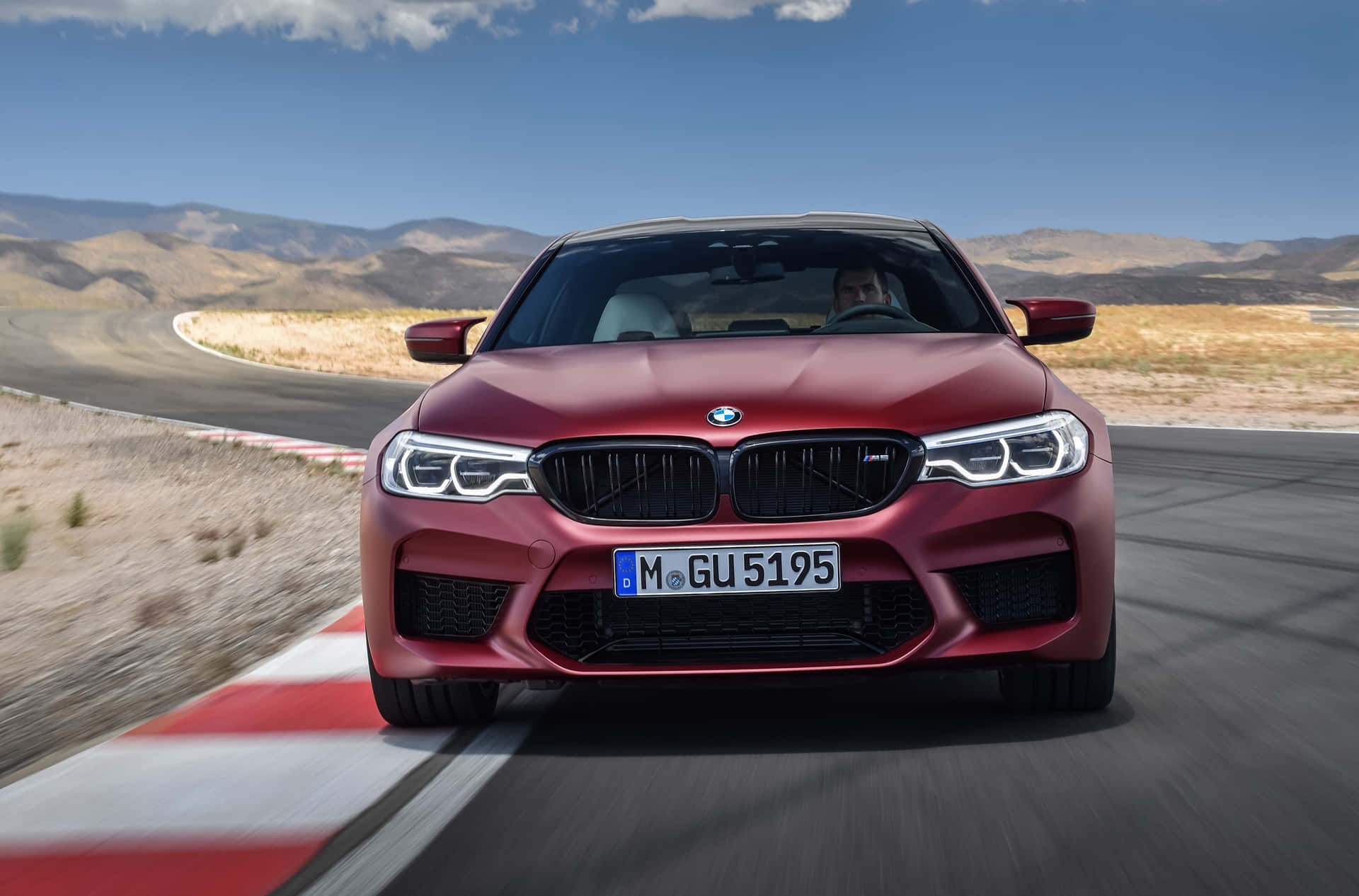 紅色BMW M5在沙漠賽道上疾馳，背景有山脈。