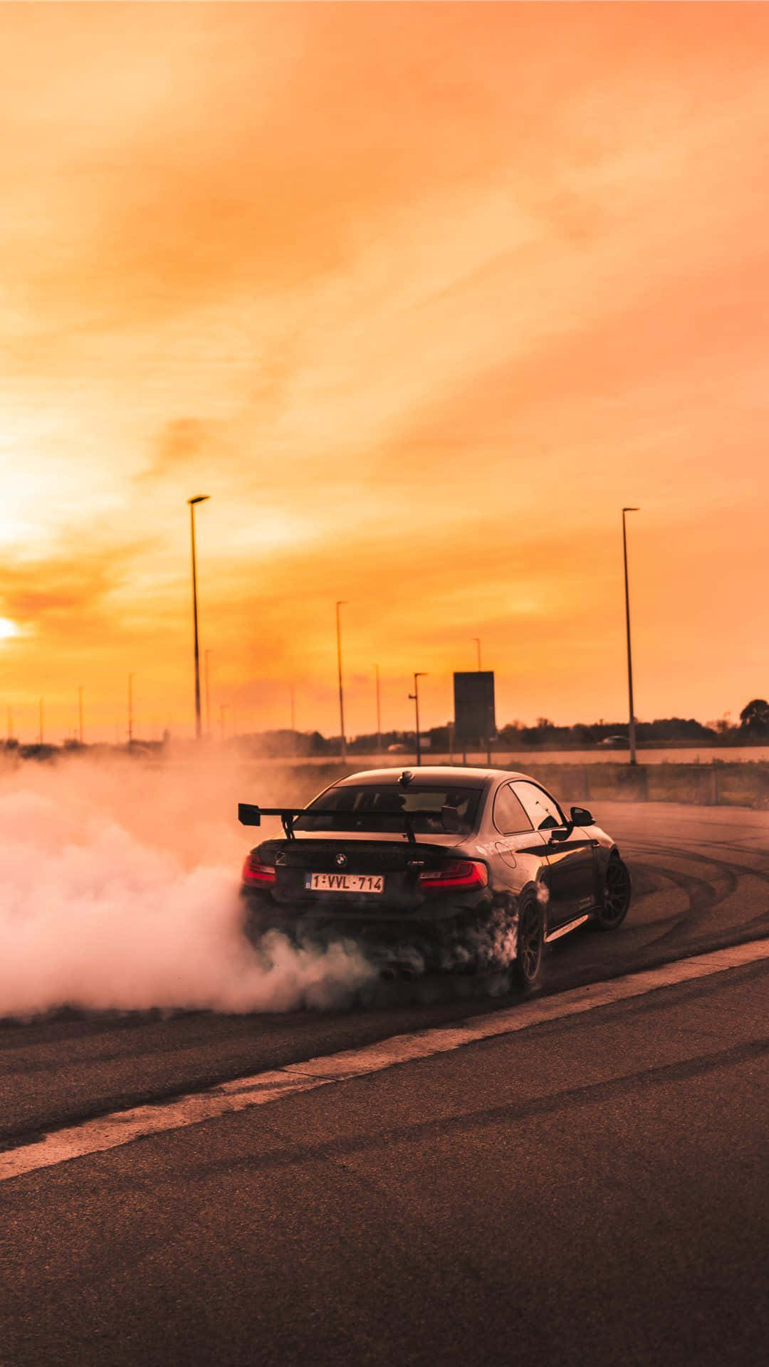 BMW M5漂移經典車 壁紙 — 一輛黑色跑車在空無一人的道路上日落時分飄移，揚起濃煙，映襯著火紅的橙色天空。