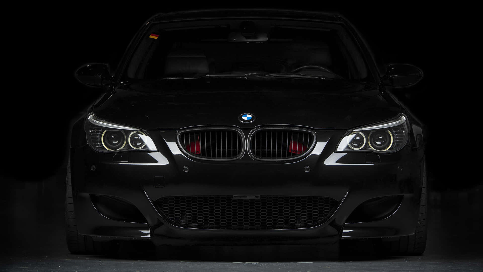黑色BMW跑車正面視圖，車頭燈在黑暗的工作室中發光。