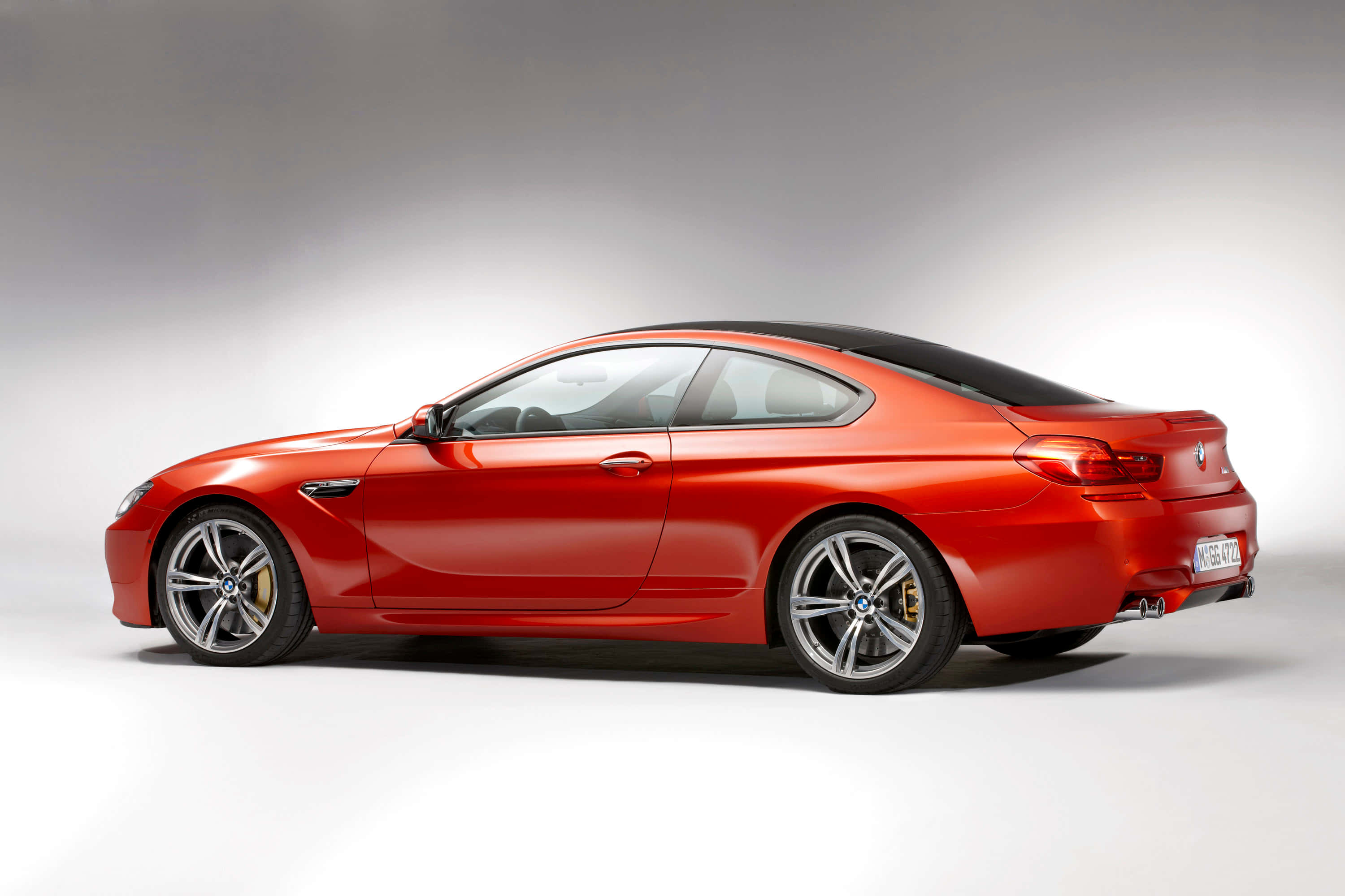流線型強勁的 BMW M6 駛於開放道路 壁紙 — 一輛時尚的紅色BMW M6雙門轎跑車，配備黑色車頂和金色制動卡鉗，在工作室側面展示。
