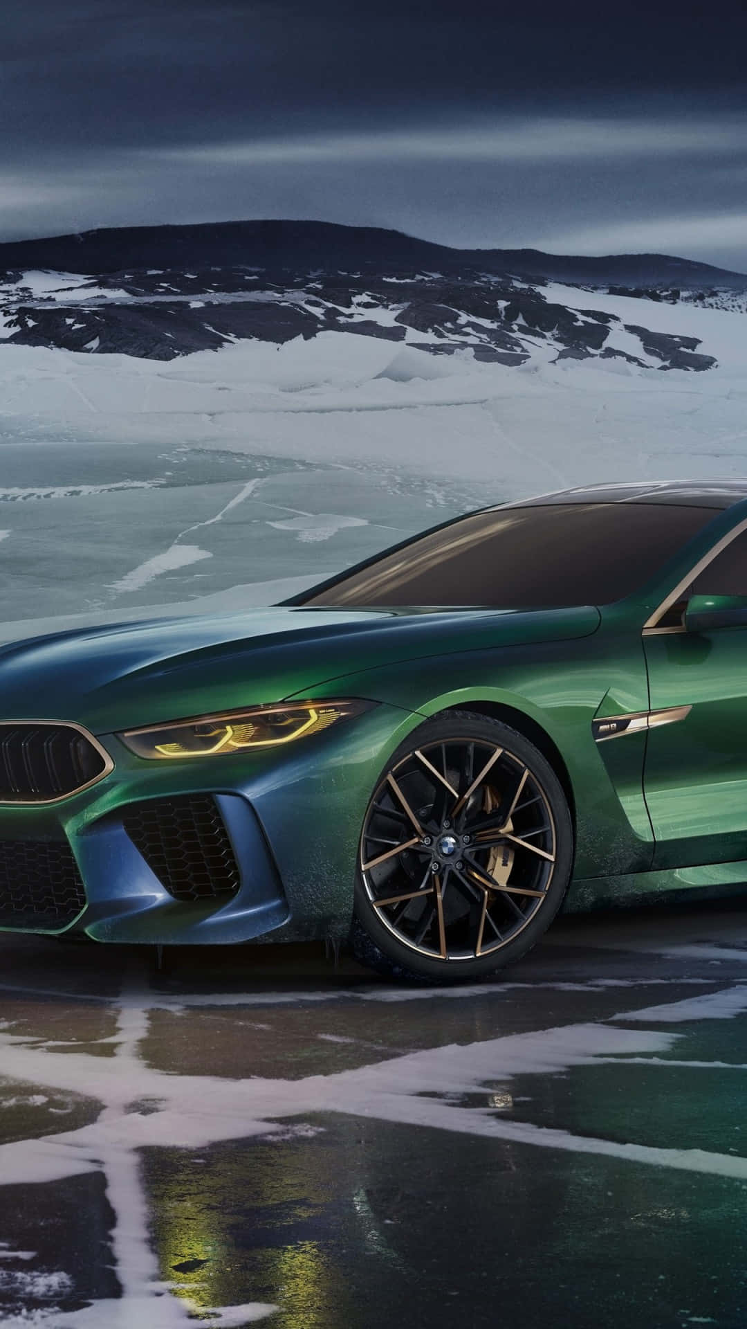 綠色BMW M8 Coupe停放在冰凍的湖面上，背景有積雪的山脈。