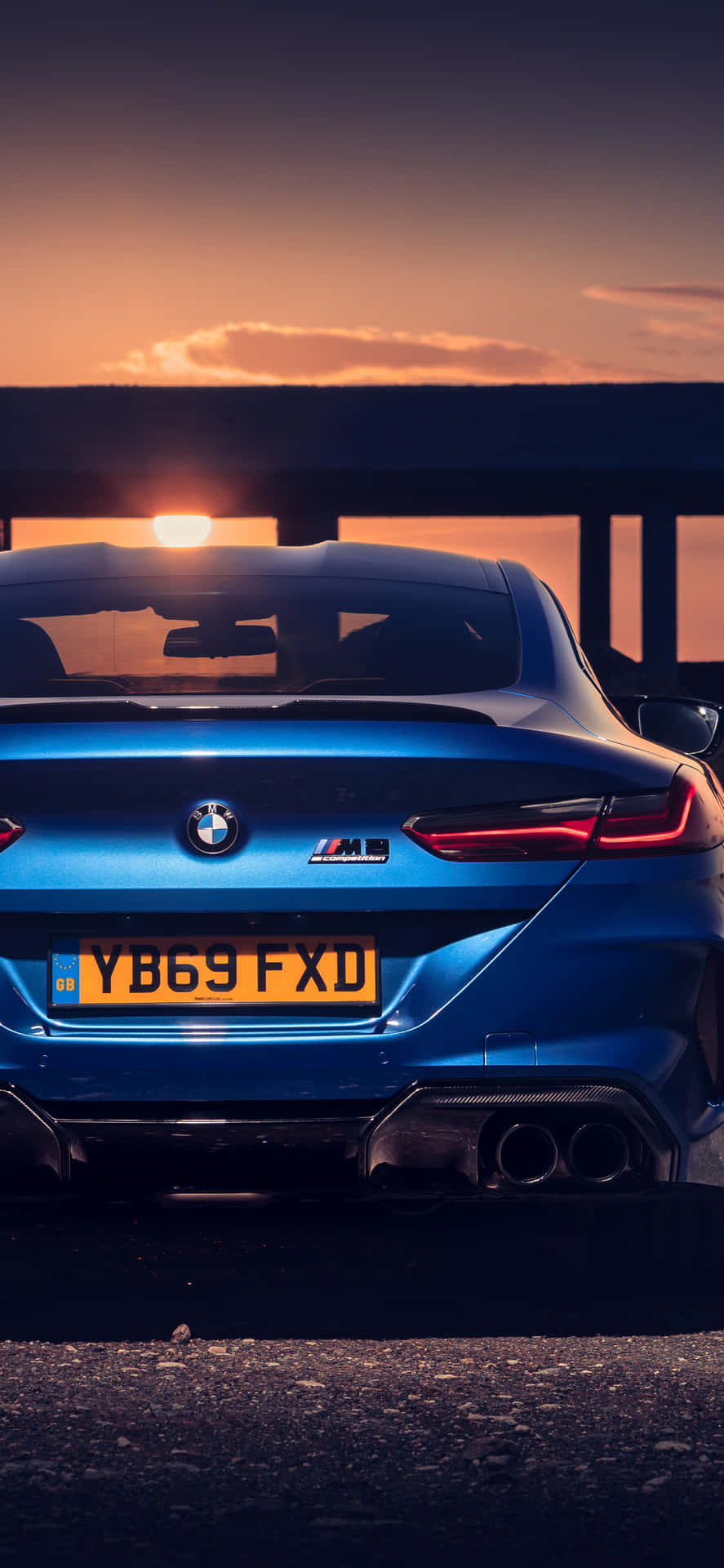 日落時分的藍色BMW M8 Coupe，帶有發光的尾燈和溫暖的天空。