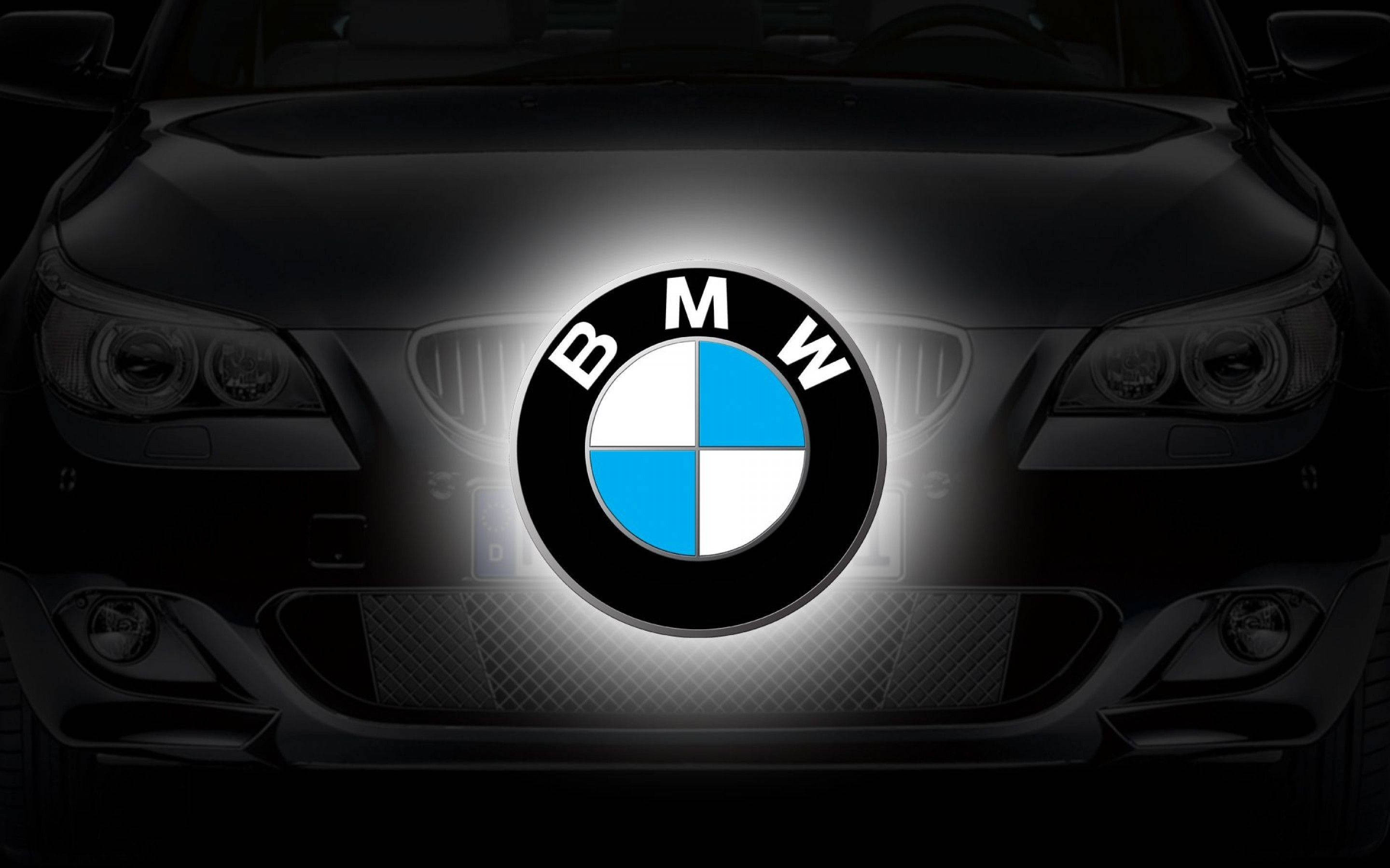 BMW M系列跑車標誌 壁紙 — 黑色寶馬汽車的前格柵在黑暗背景下發出明亮的光芒，帶有發光的標誌。