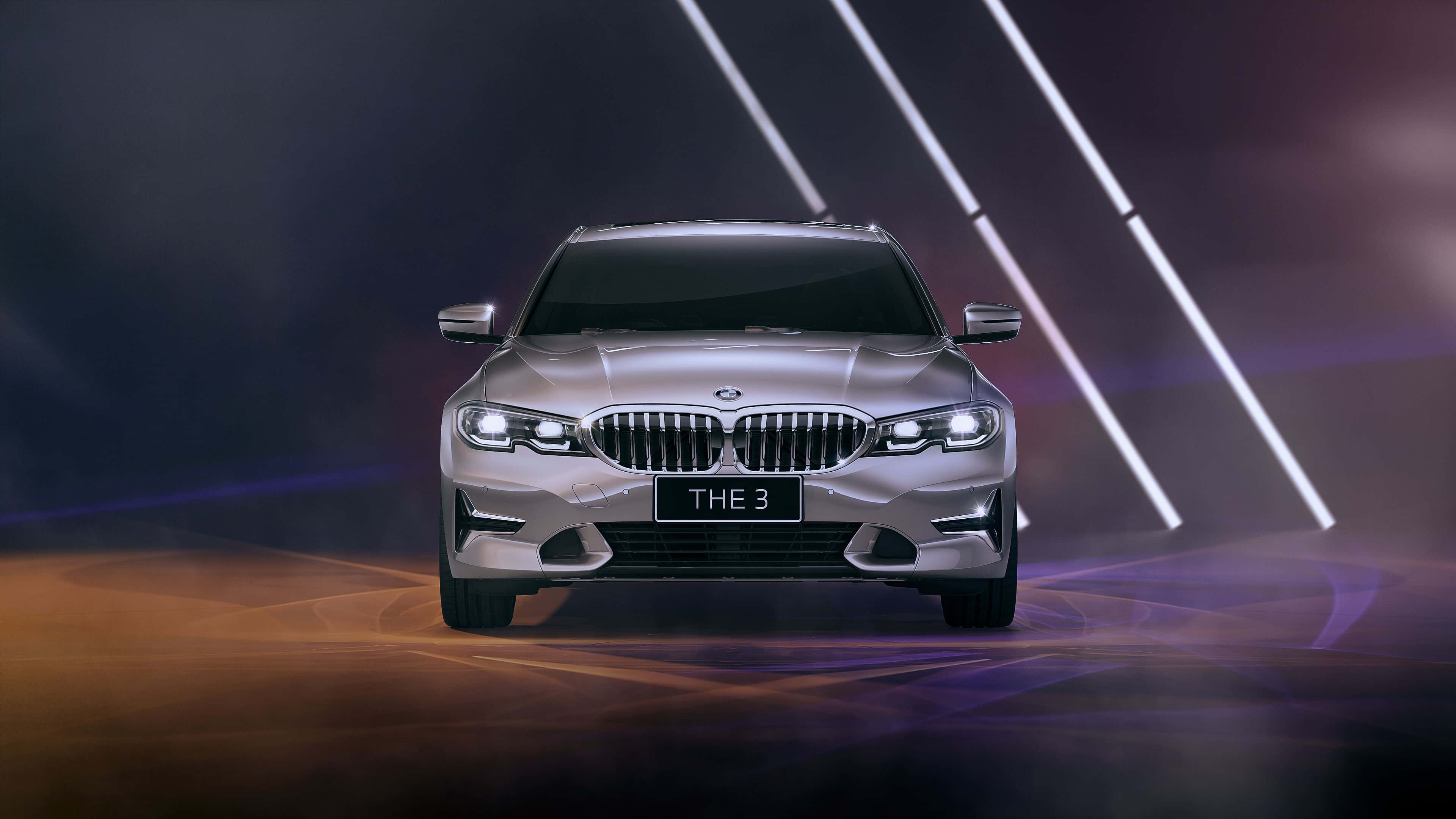 奢華銀色BMW白光 壁紙 — 一架時尚的銀色寶馬3系轎車在煙霧彌漫的舞台上，在戲劇性的對角聚光燈下正面展示，伴隨著旋轉的橙色和紫色地面效果。