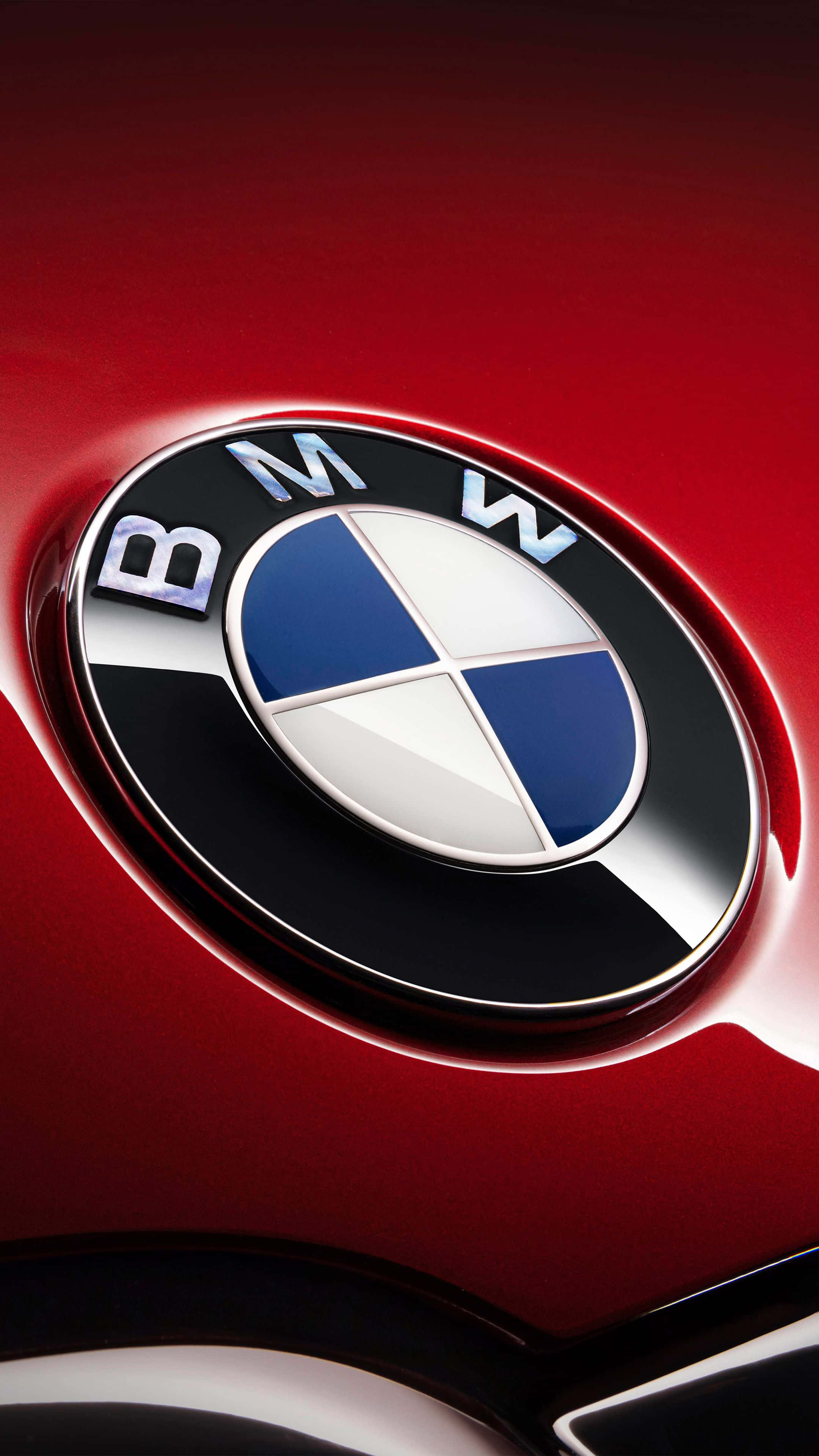 搭載最新安卓科技的BMW SUV 壁紙 — 近距離拍攝的亮面紅色BMW標誌，帶有藍白相間的區域，反射出攝影棚燈光。