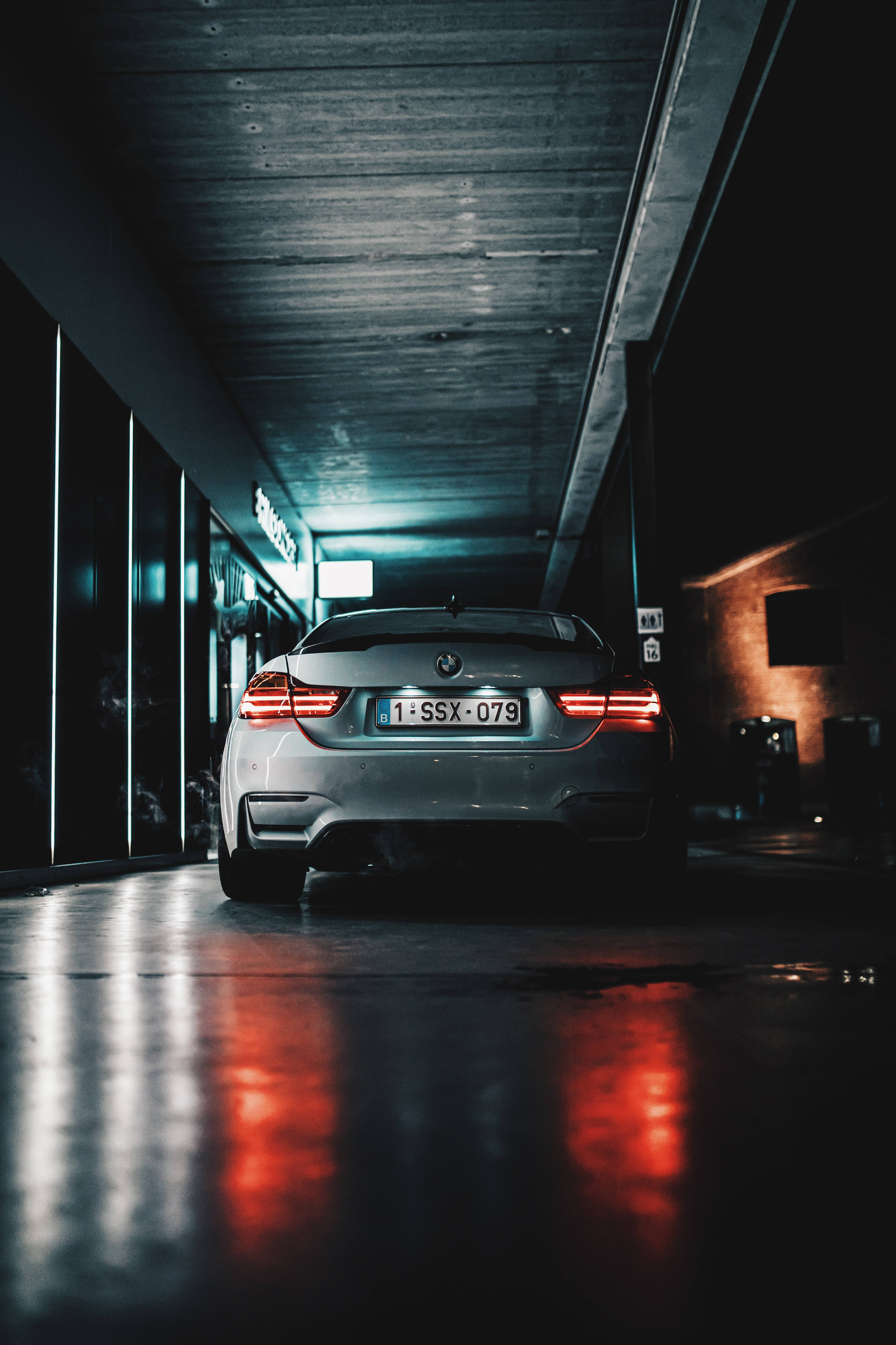 霓虹BMW跑車 壁紙 — 一輛銀色寶馬房車的紅色尾燈在夜間昏暗的城市天橋下，在濕漉漉的路面上反射出光芒。