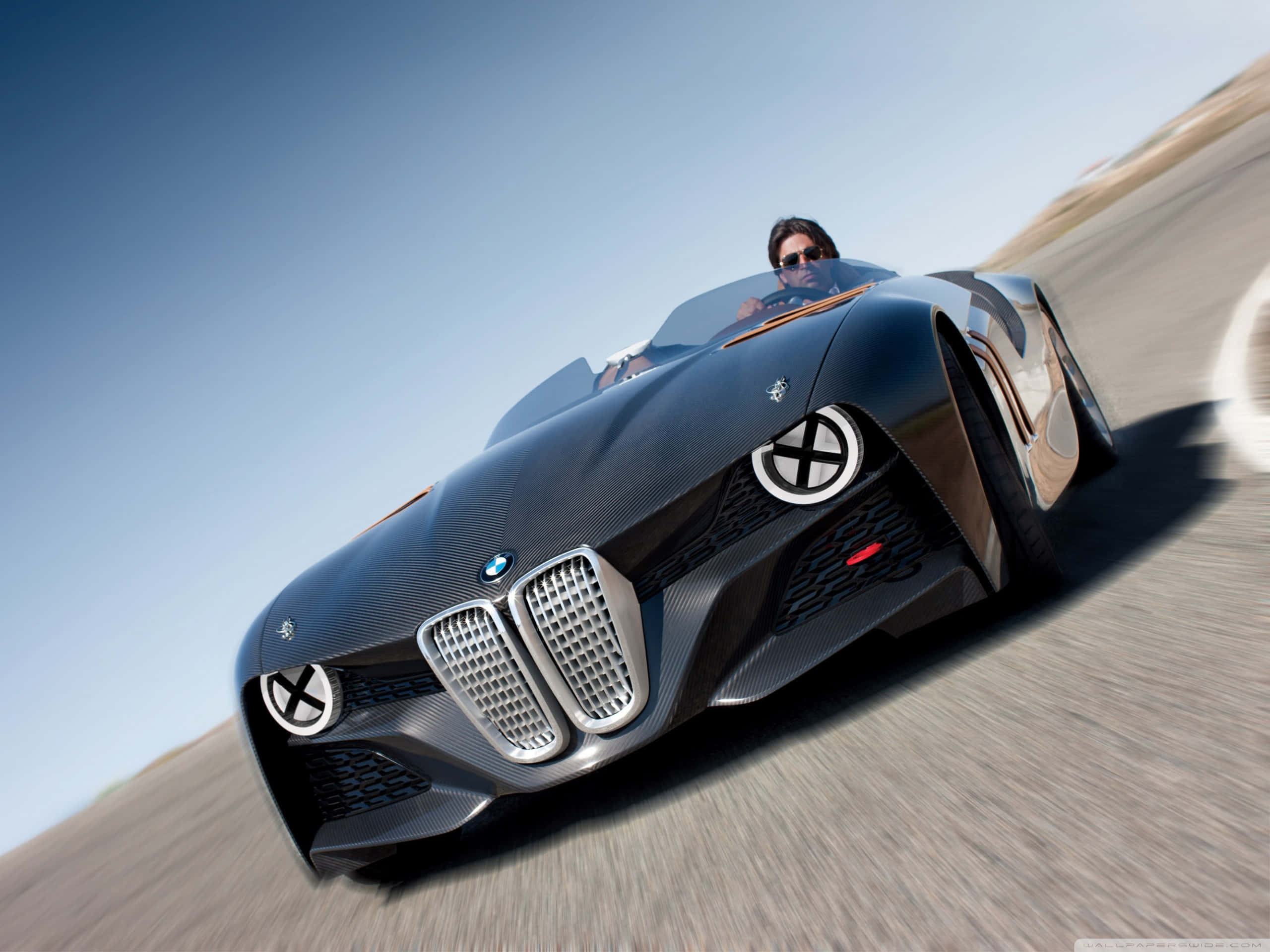 經典 BMW 風格 壁紙 — 一輛時尚的黑色BMW概念車在晴朗藍天下沿沙漠道路疾馳，司機戴著太陽眼鏡。