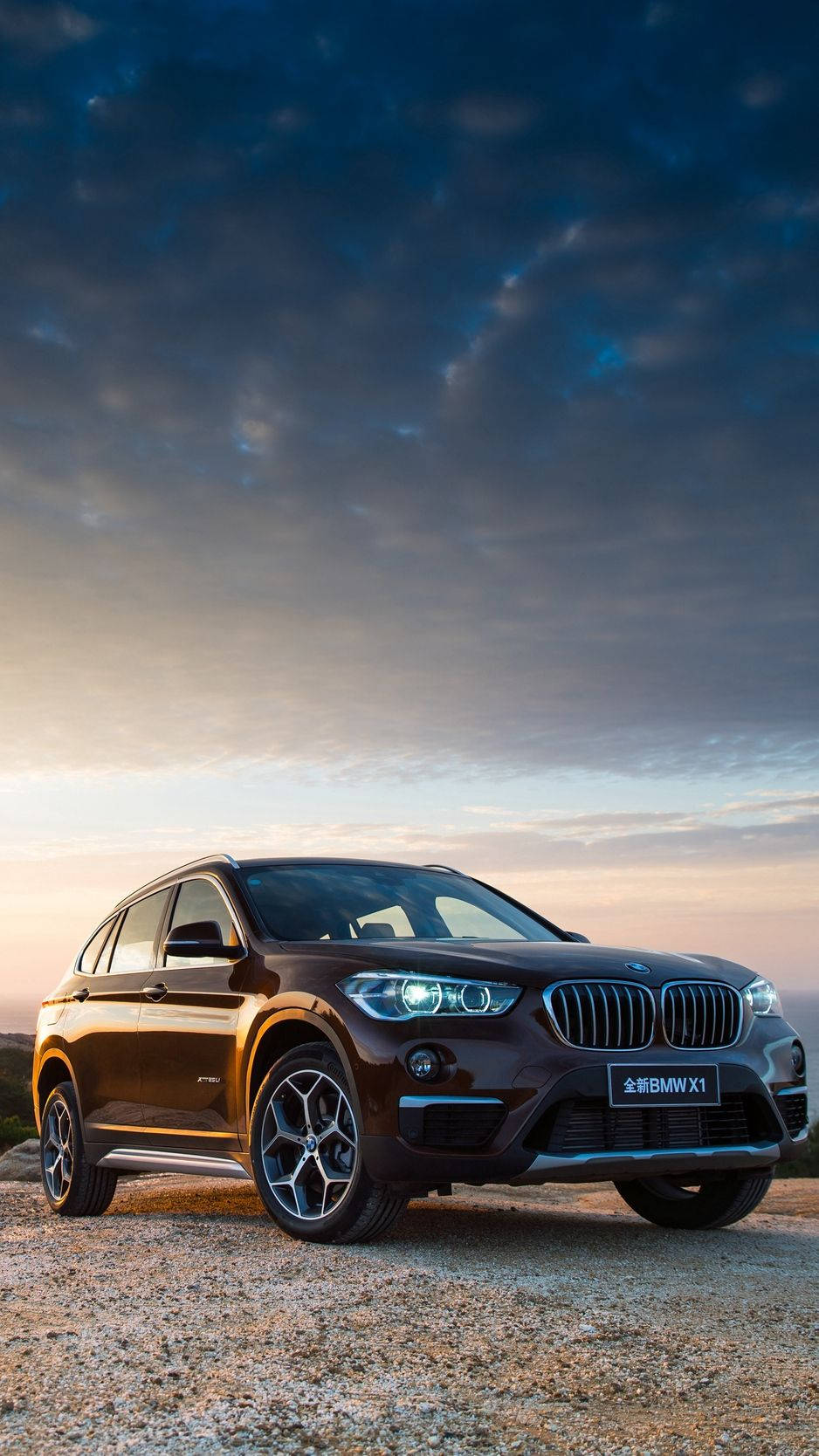 日落時分，碎石上的棕色BMW X1 SUV，車頭燈閃閃發光。