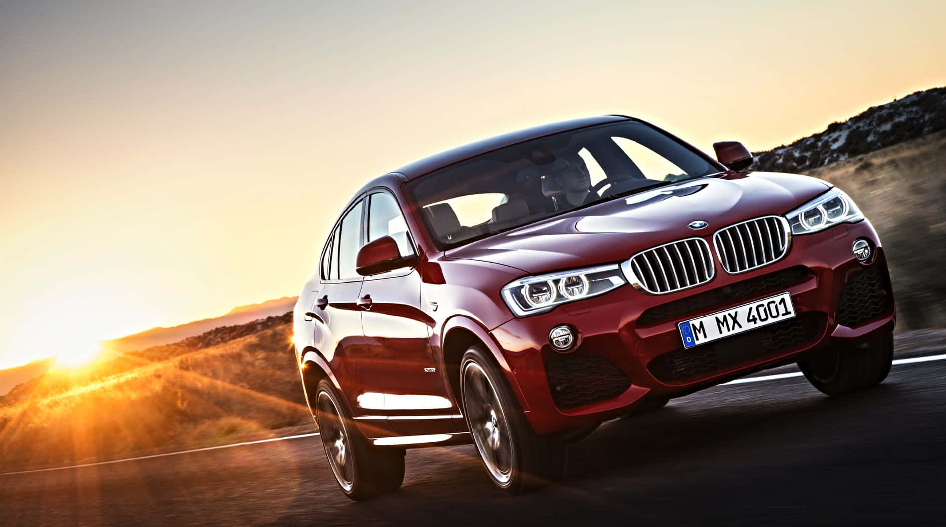 BMW X4：時尚與性能的完美融合 壁紙 — 一輛亮紅色BMW X4 SUV在日落時分沿沙漠公路飛馳，背後太陽散發出金色光芒。