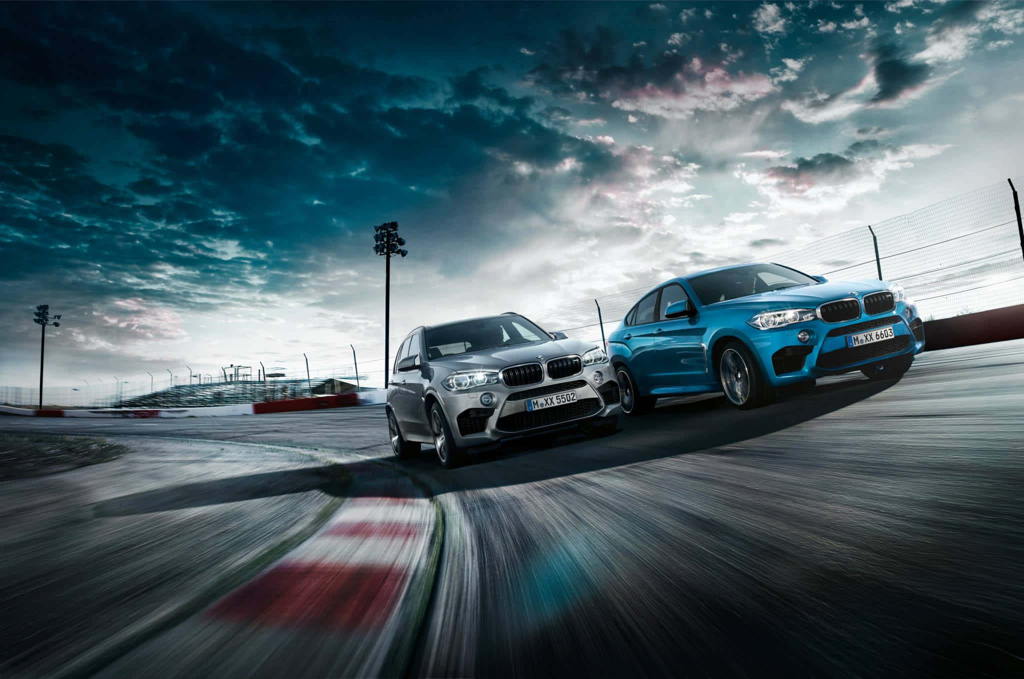 全新 BMW X6 M — 無與倫比的豪華與性能 壁紙 — 兩輛BMW SUV在戲劇性的多雲天空下並排競速，帶有動態模糊效果。