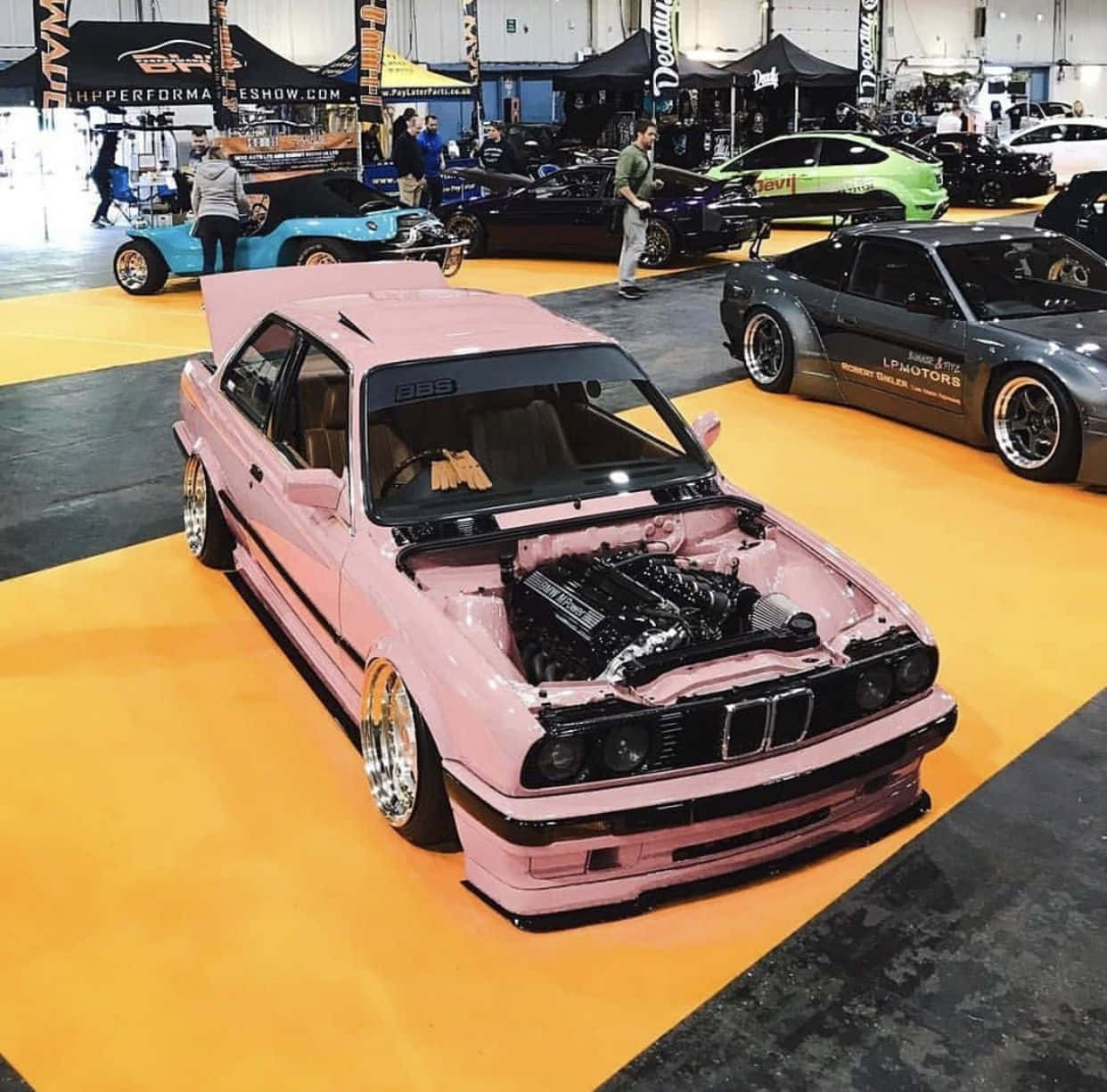奢華的未來已至，BMW X6 M Competition 壁紙 — 一輛鮮粉紅色改裝BMW E30打開引擎蓋，在室內車展中展示定制引擎。