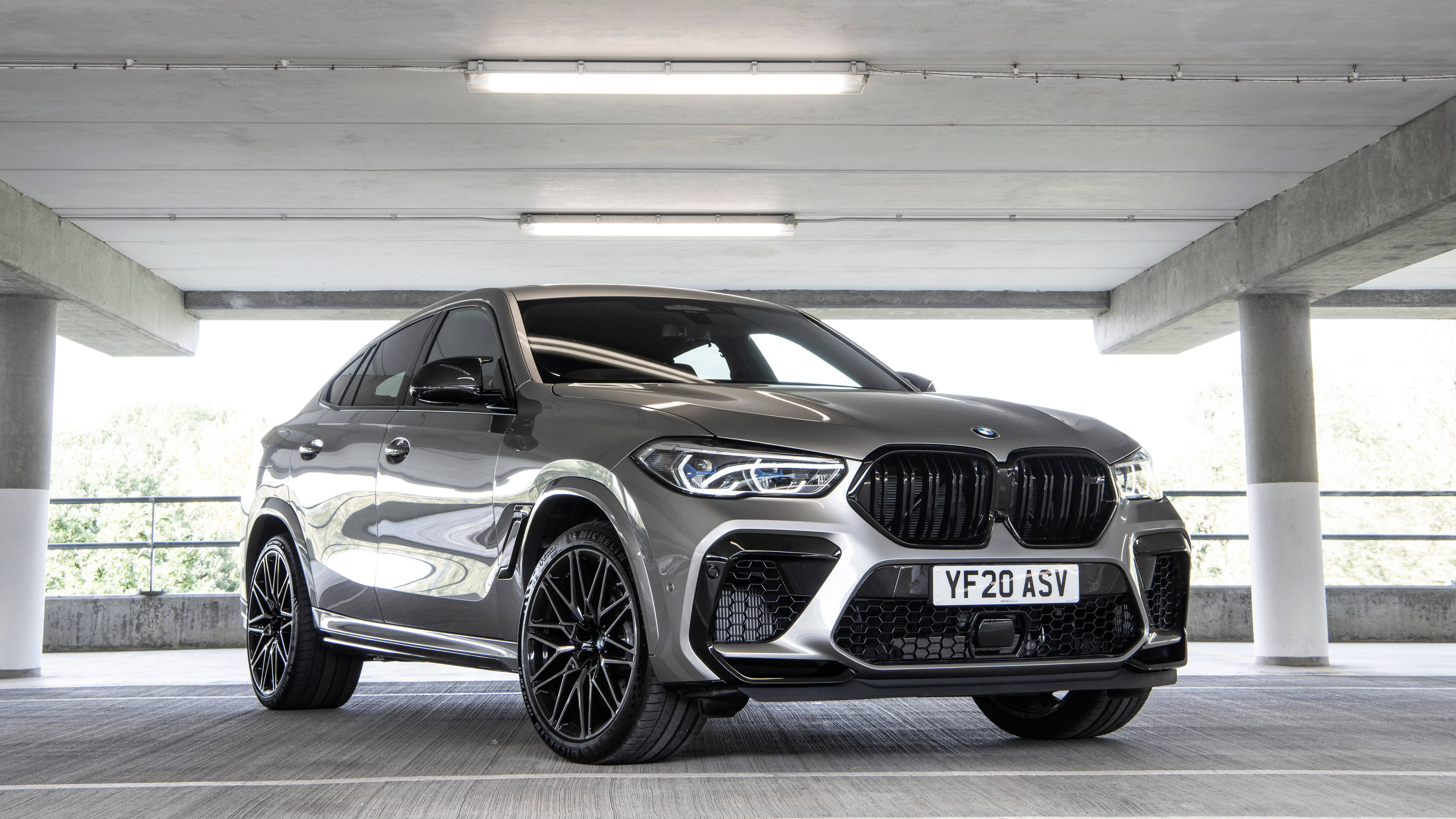 BMW X6 M 停車場 壁紙 — 一輛時尚的銀色BMW X6 M停在混凝土停車場下，明亮的頂燈反射在其拋光表面上。