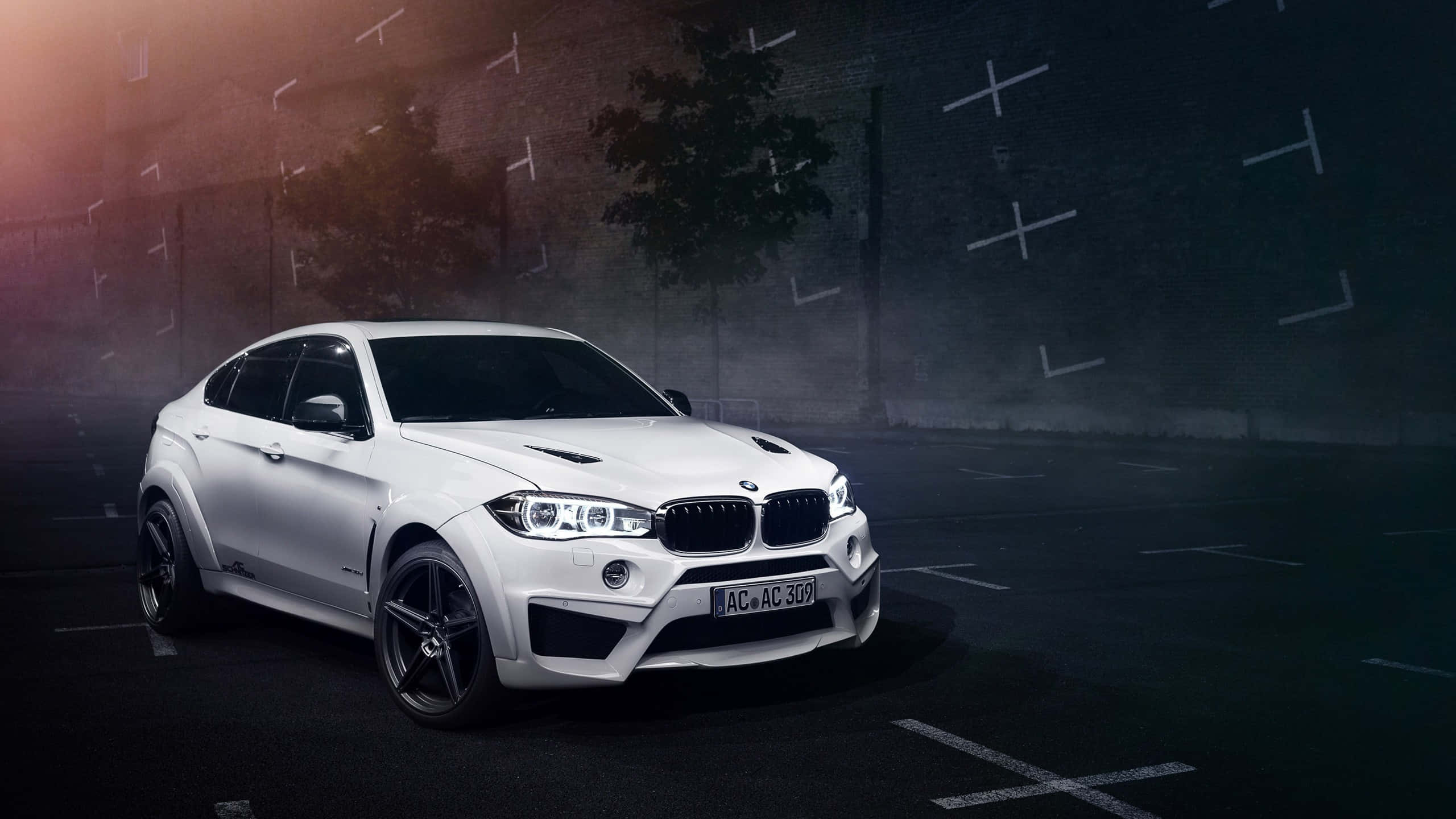 BMW X6 M — 奢華運動休旅車的巔峰之作 壁紙 — 一架時尚的白色BMW X6M跑車在空蕩的城市停車場中，在戲劇性的夜間燈光下閃閃發光。