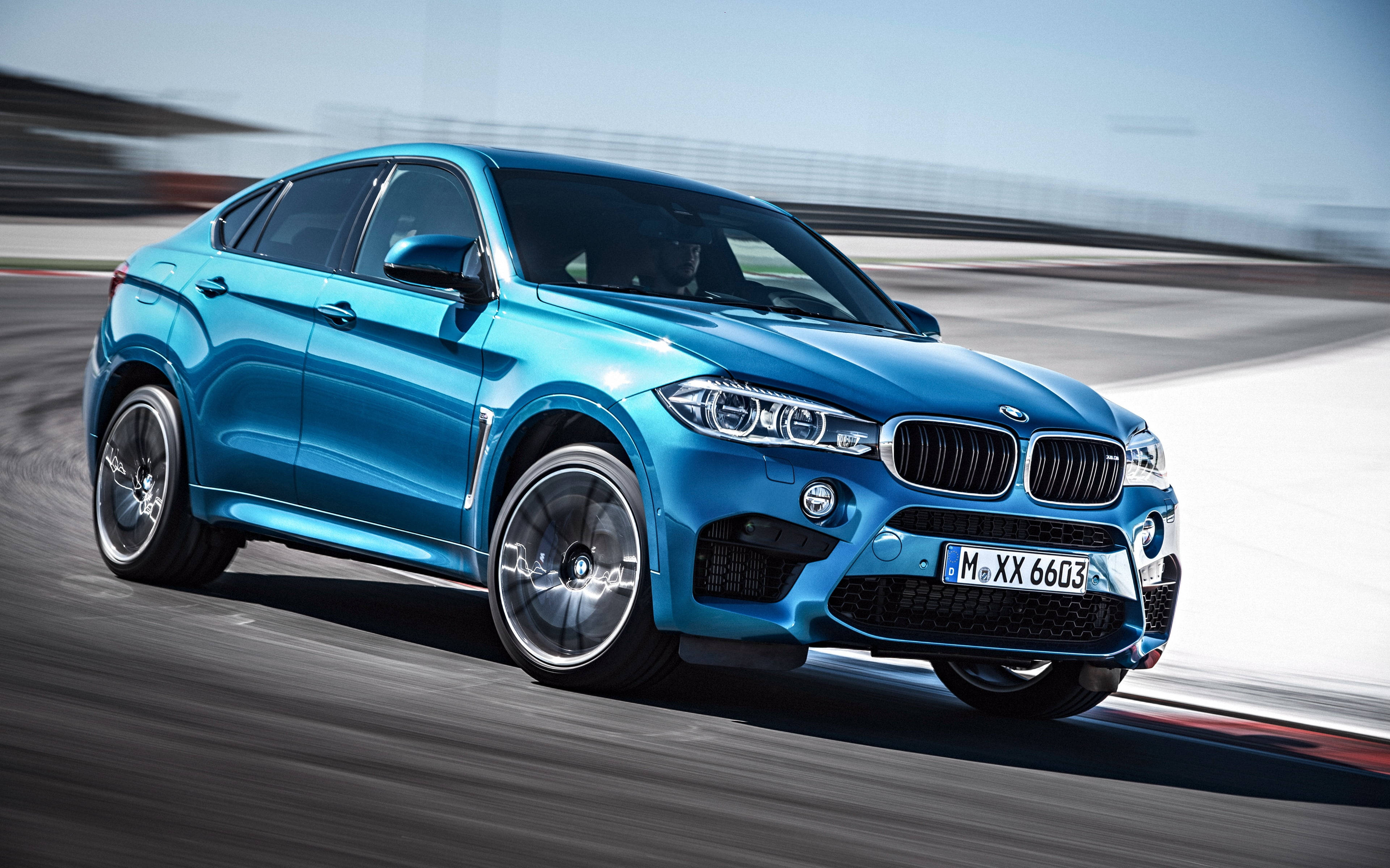 BMW X6 M 雪地道路 壁紙 — 一輛充滿活力的藍色BMW X6 M在賽道上疾馳，動態模糊效果凸顯其力量和時尚設計。