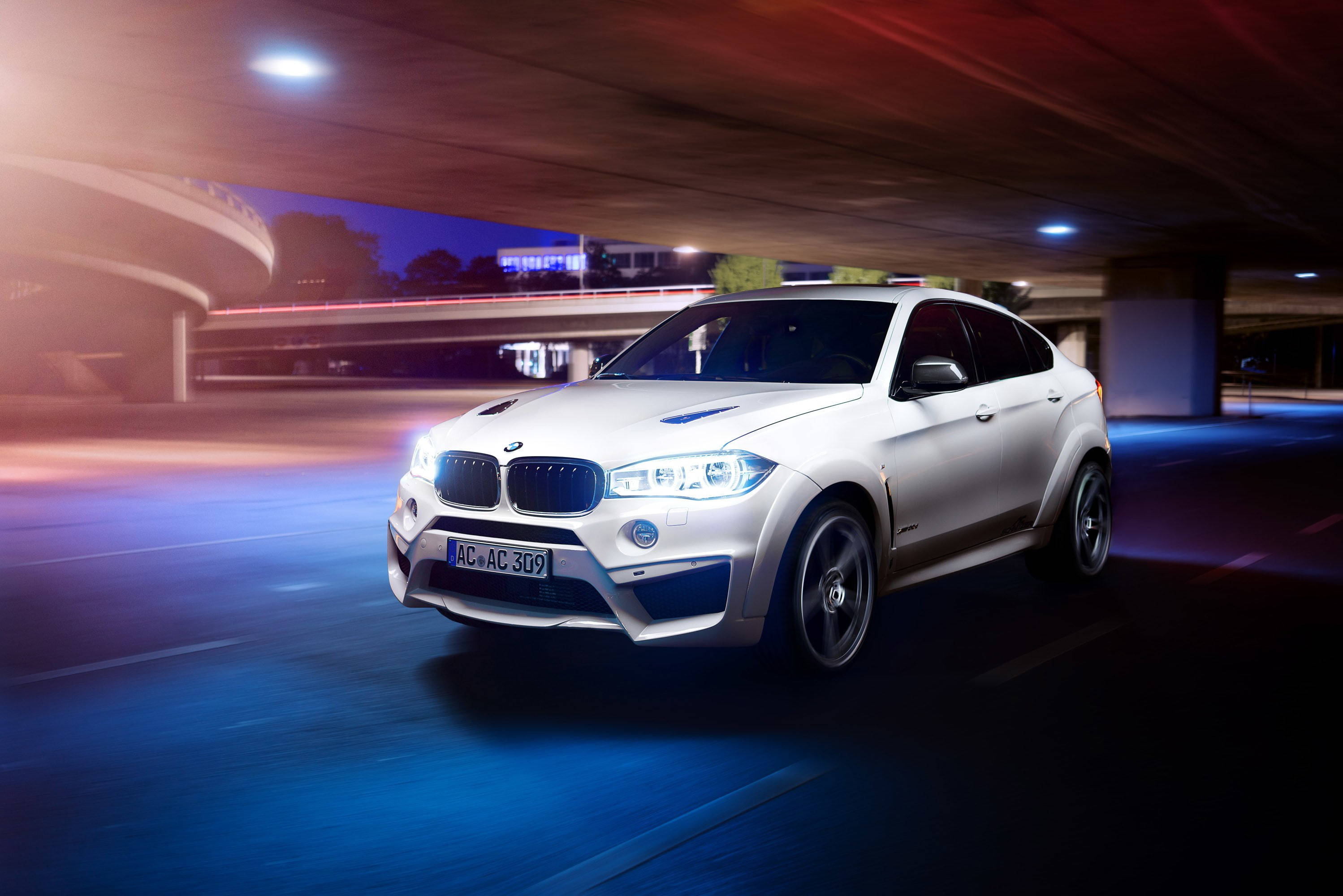 BMW X6 M停於高架橋下 壁紙 — 一輛白色BMW X6 M在夜間於發光的城市高架橋下疾馳，帶有藍色和紅色光的動態模糊條紋。
