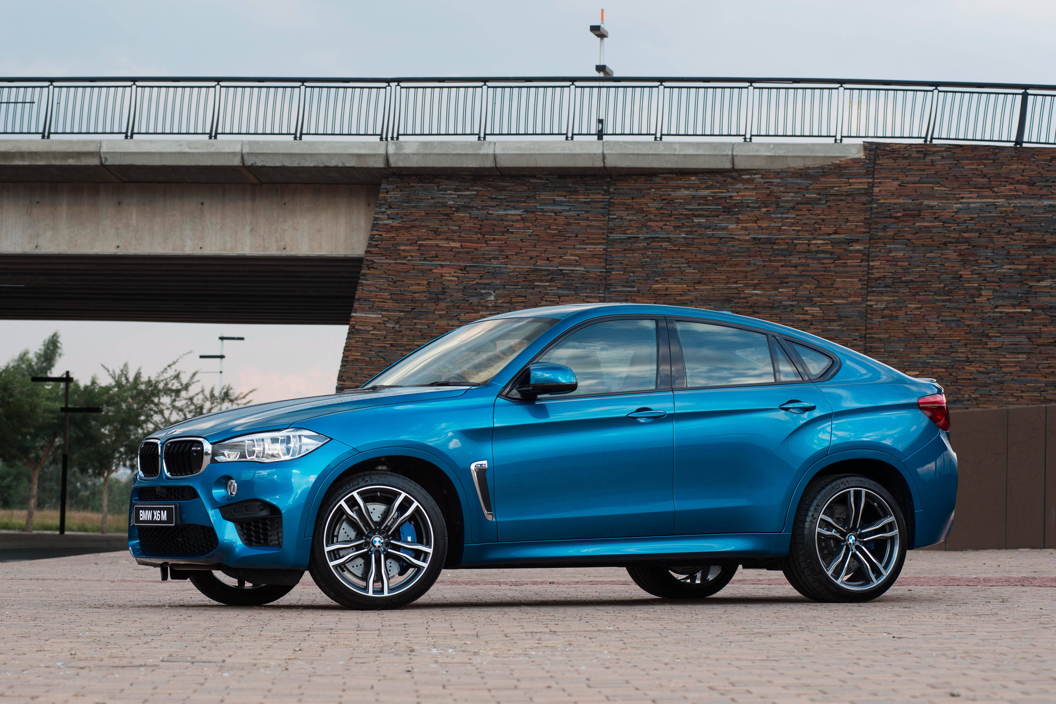 BMW X6 M停於高架橋下 壁紙 — 一輛鮮藍色BMW X6M SUV停泊在混凝土橋下，背景為石牆。