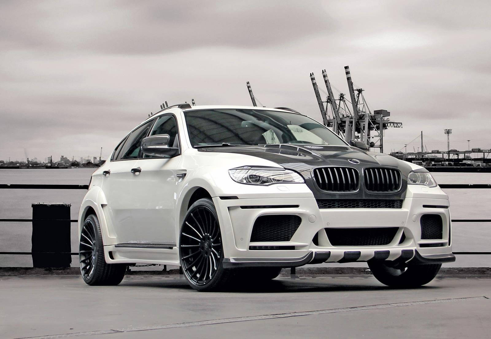 BMW X6 M停泊碼頭 壁紙 — 一輛白色改裝寶馬X6運動型多功能車，帶有黑色飾邊，停泊在工業起重機附近的碼頭，天空多雲。
