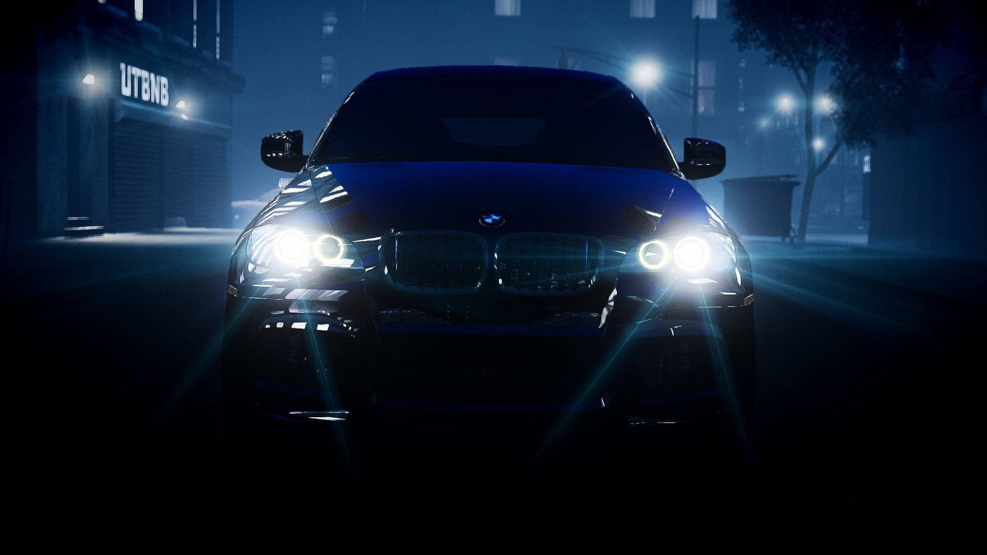 BMW X6 M前大燈特寫 壁紙 — 一輛時尚的黑色BMW SUV在夜間主導著霧氣瀰漫的城市街道，明亮的車頭燈劃破迷霧，背景中路燈閃爍。