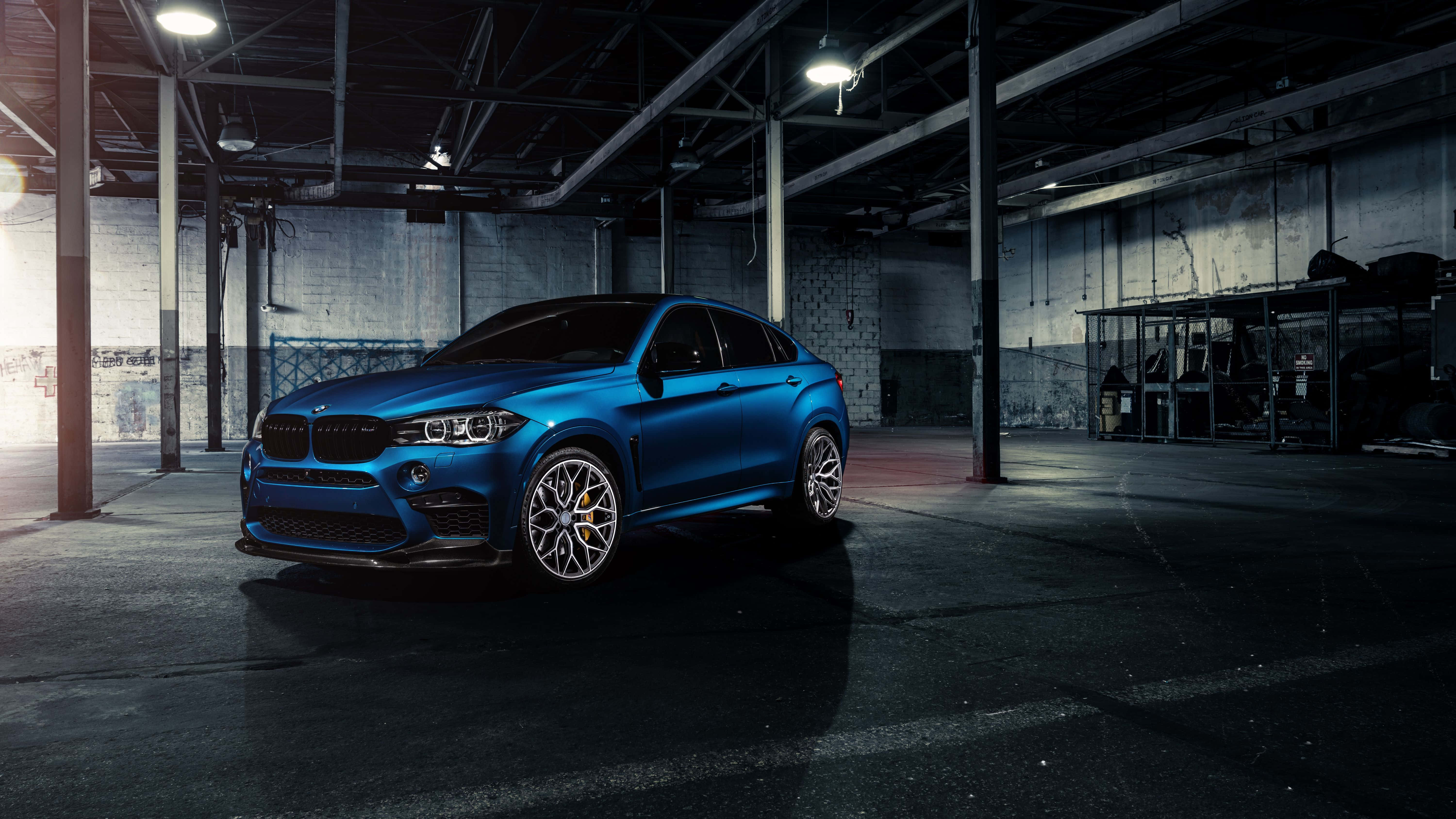 BMW X6 M在道路上提供獨特的性能與奢華體驗 壁紙 — 一輛光澤藍色寶馬X6 M Coupe在工業燈光下閃耀，身處一個有裸露橫樑和混凝土牆的粗糙倉庫中。
